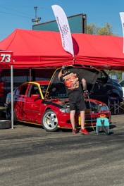 Man working on red car engine under tent