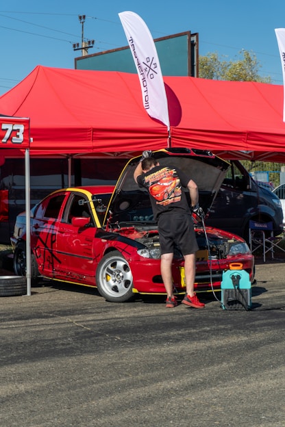 Man working on red car engine under tent