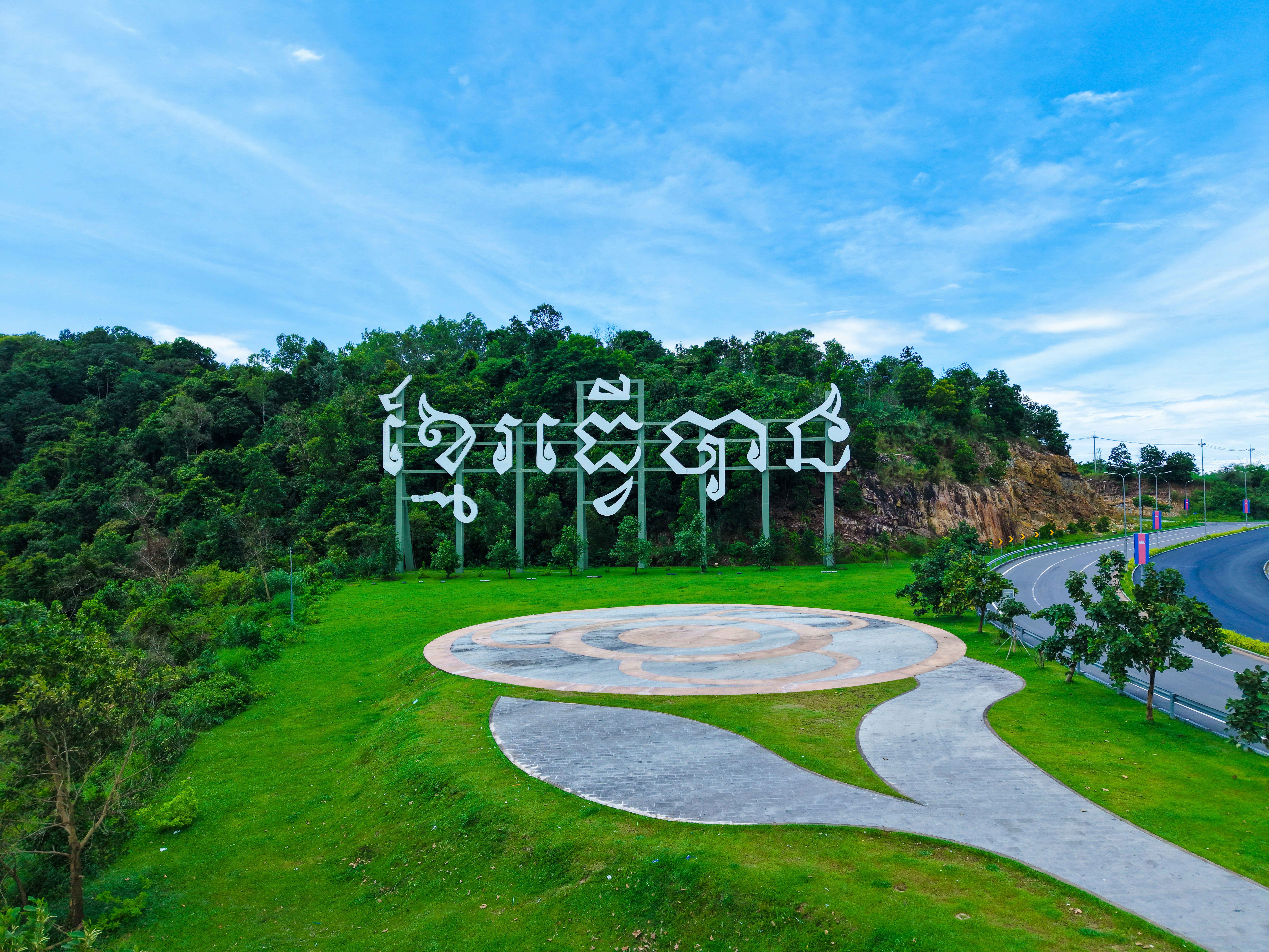 Large sign with foreign script in a green landscape.