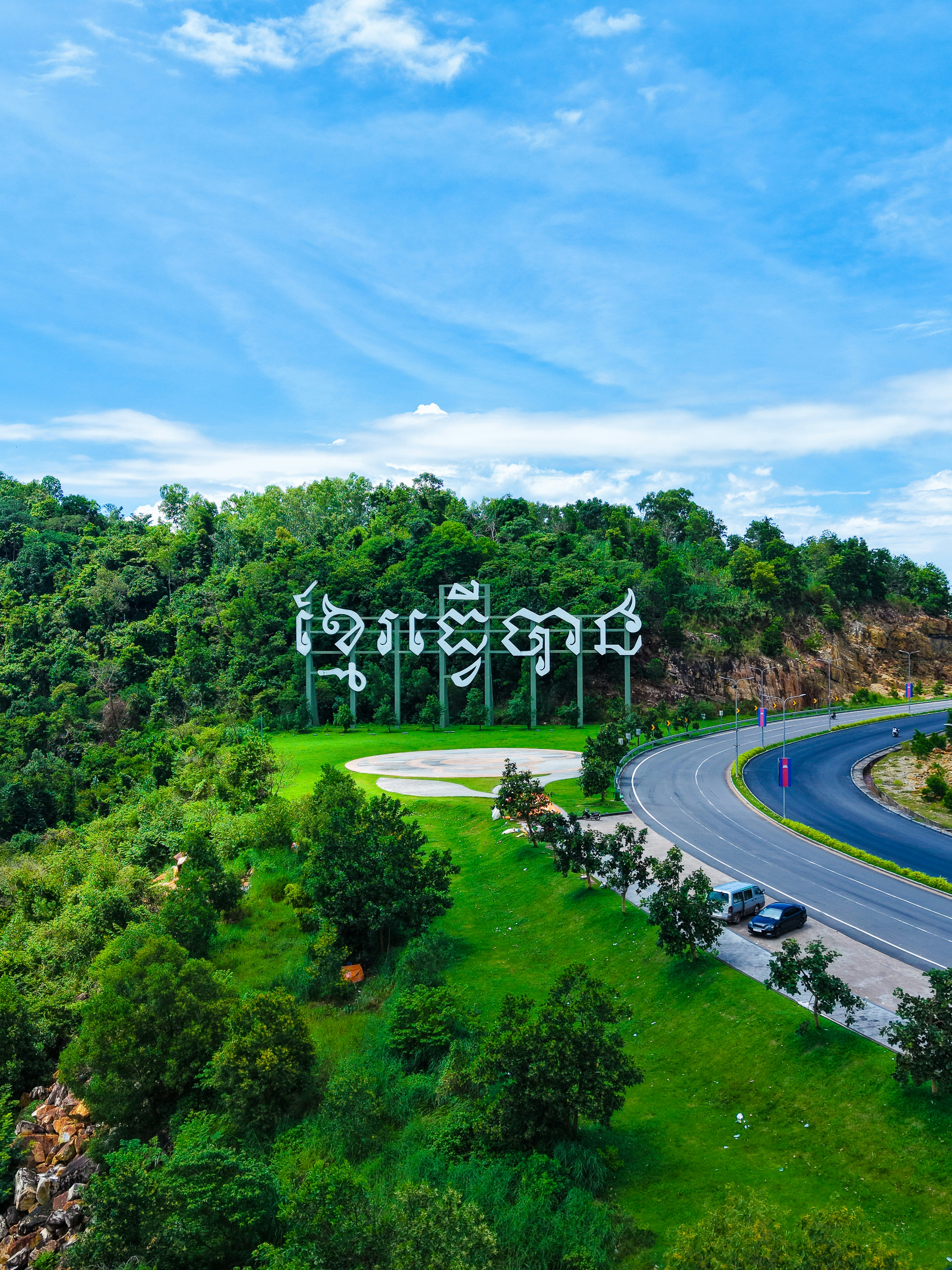 Large white lettering on a green hillside near road.