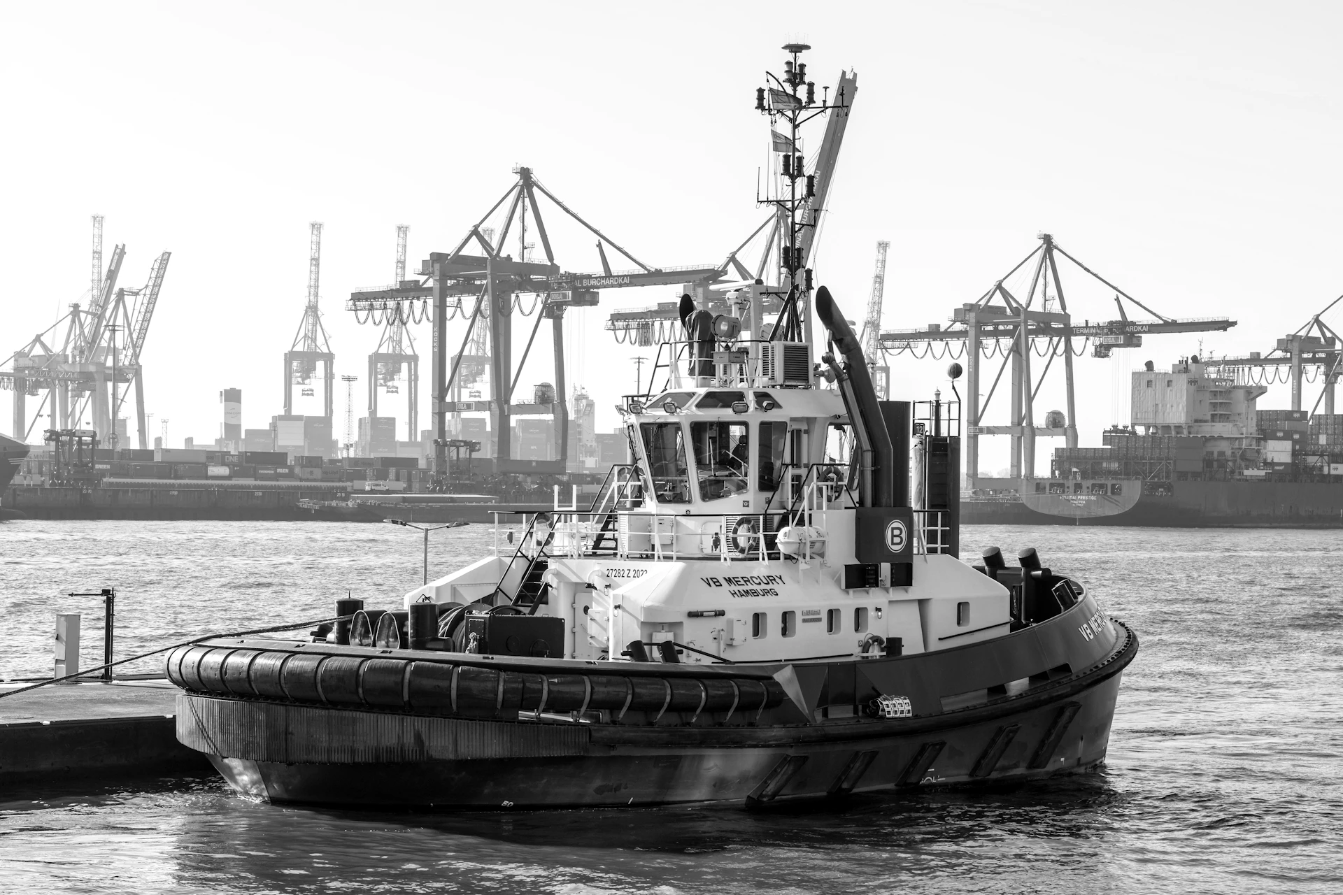Tugboat docked at a harbor with cranes in background