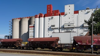 Hopper train cars in front of industrial silos and buildings.