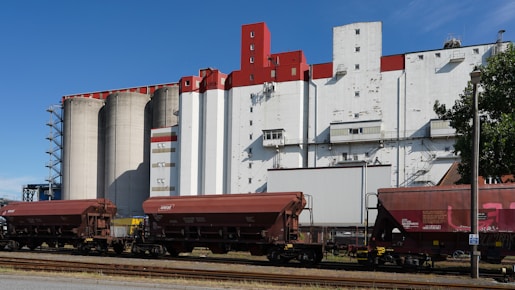 Hopper train cars in front of industrial silos and buildings.