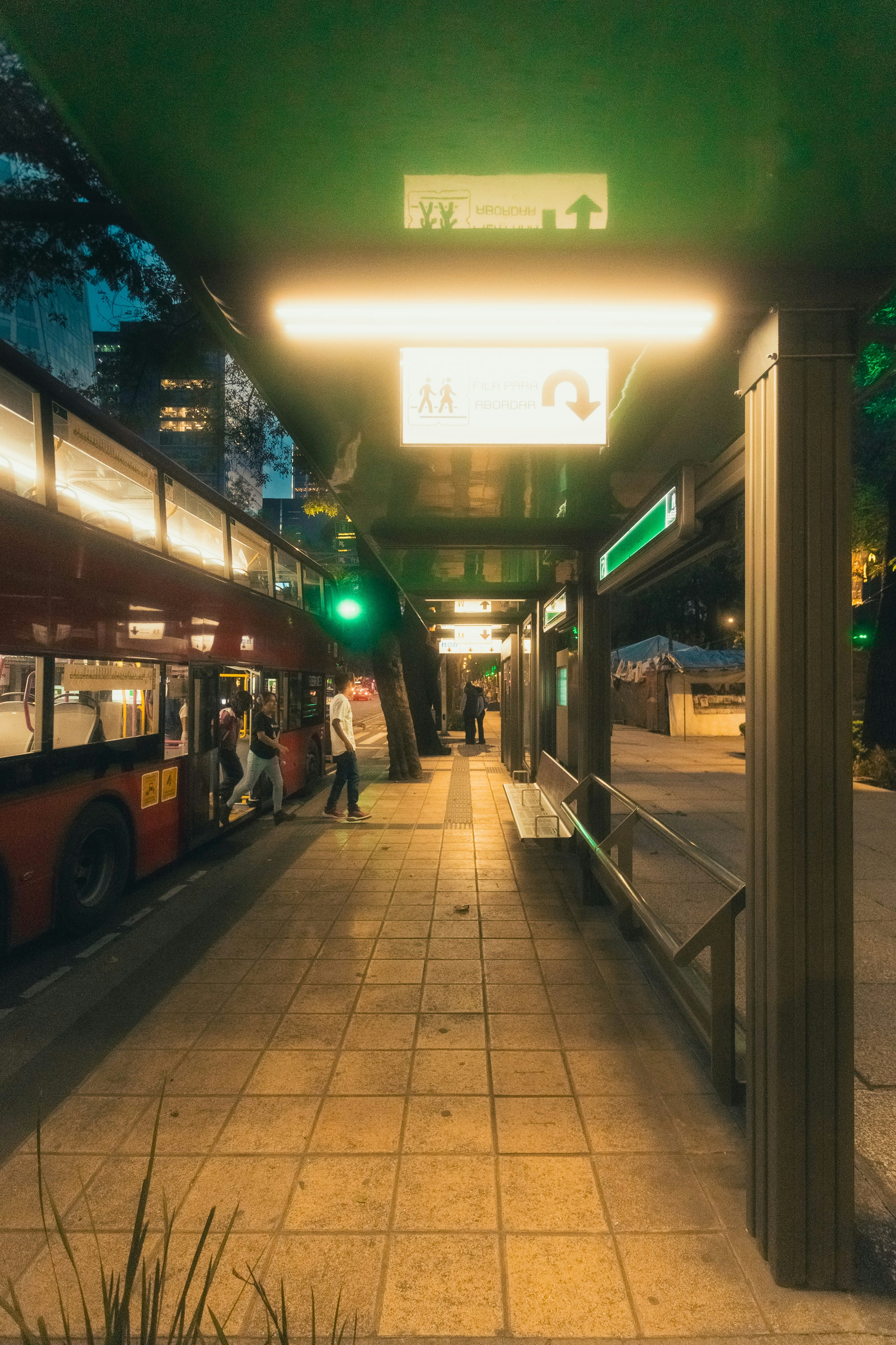 People boarding a red double-decker bus at night.