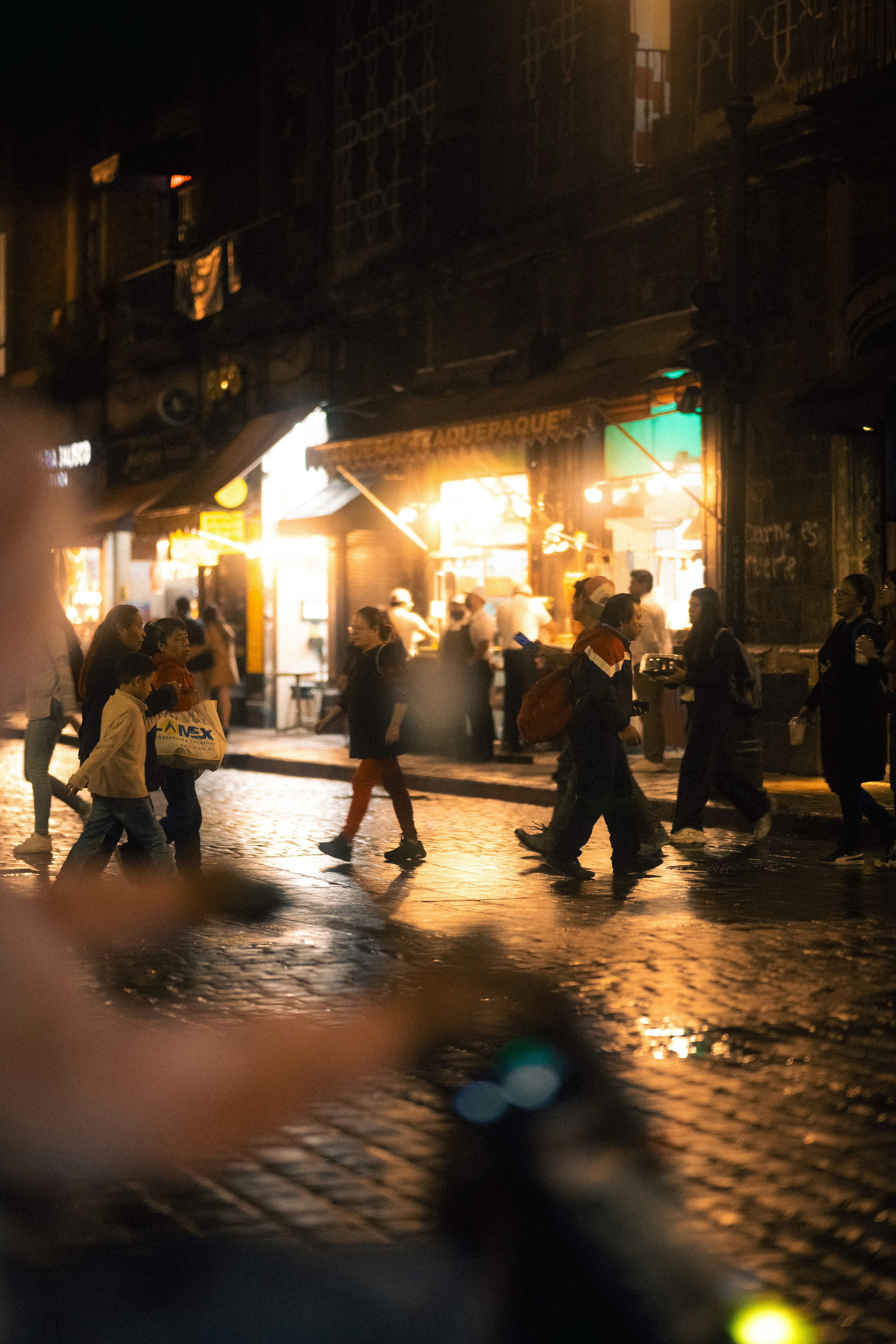 Mexico City pedestrians crossing a wet street at night, lights reflected
