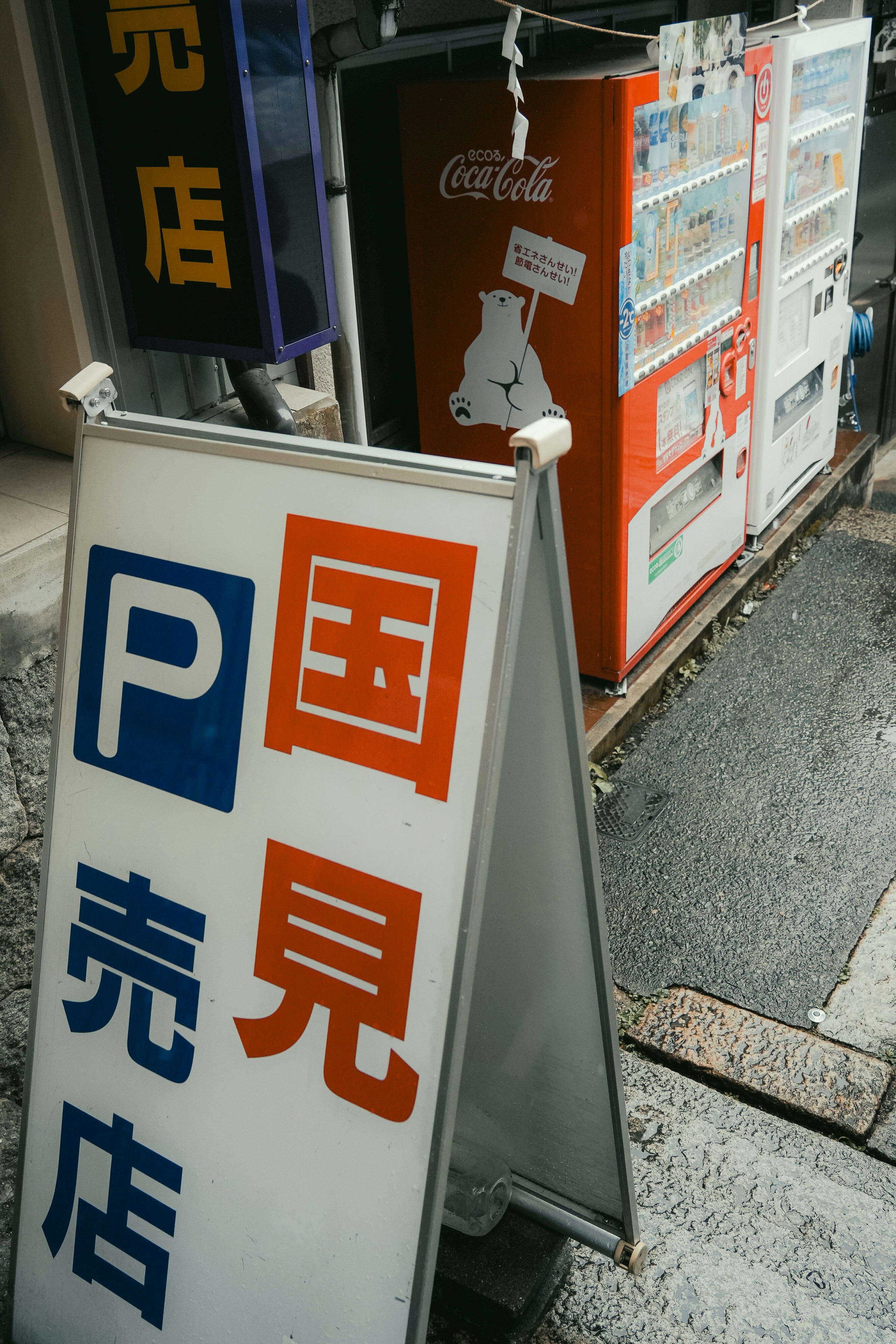 A-frame sign with japanese text and vending machines.