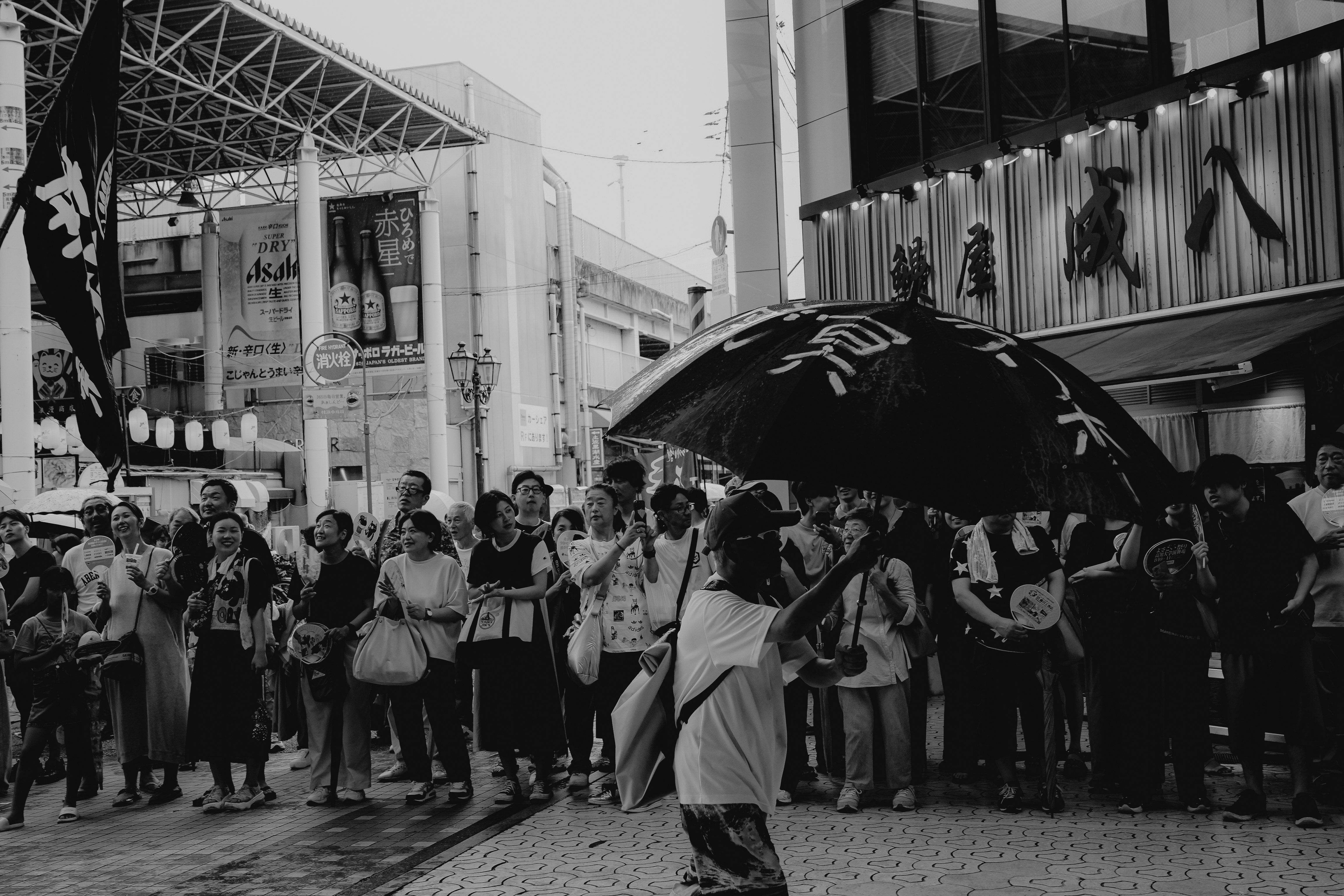 Crowd gathered on a street with umbrellas and flags