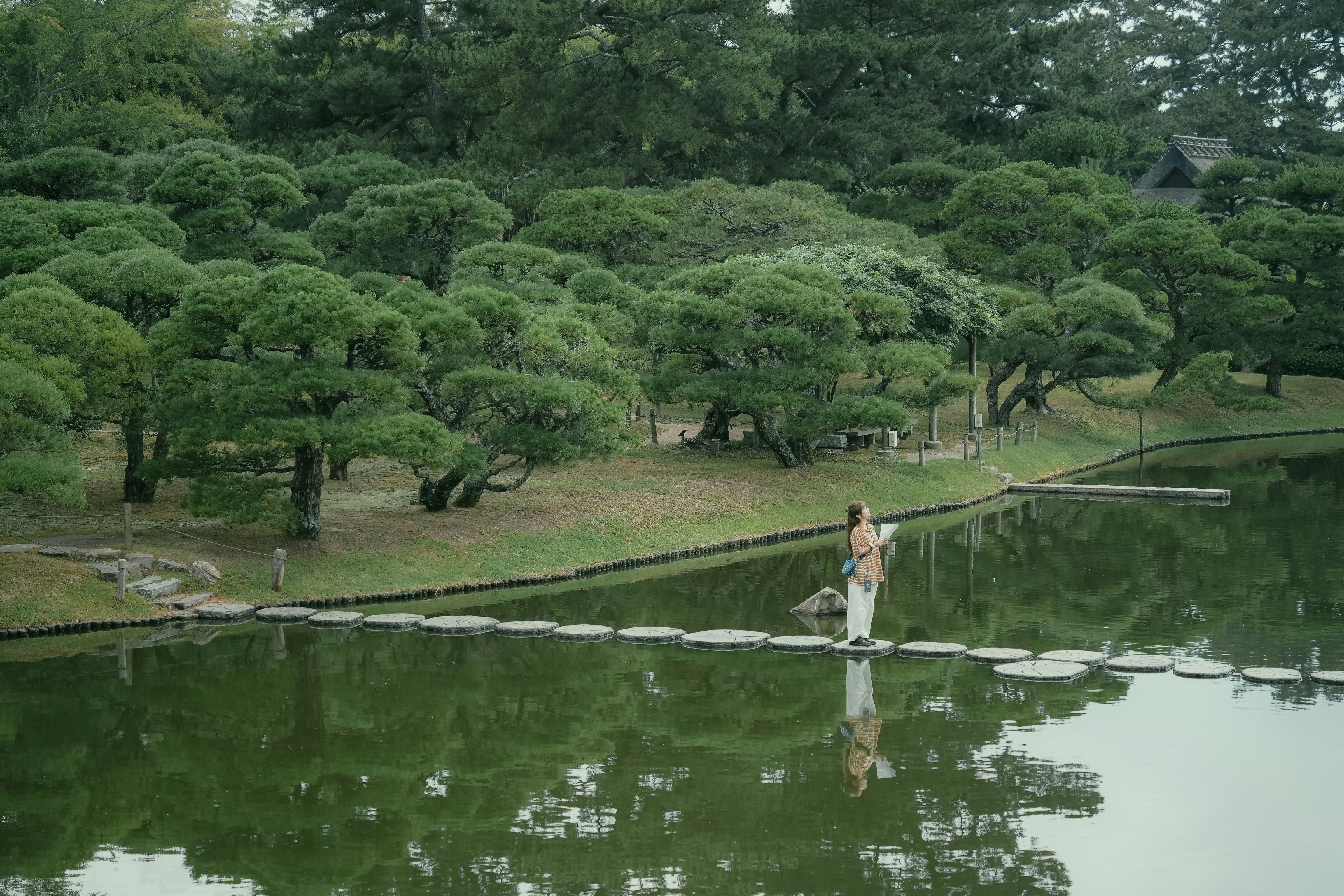 Woman walks on stepping stones across a tranquil pond