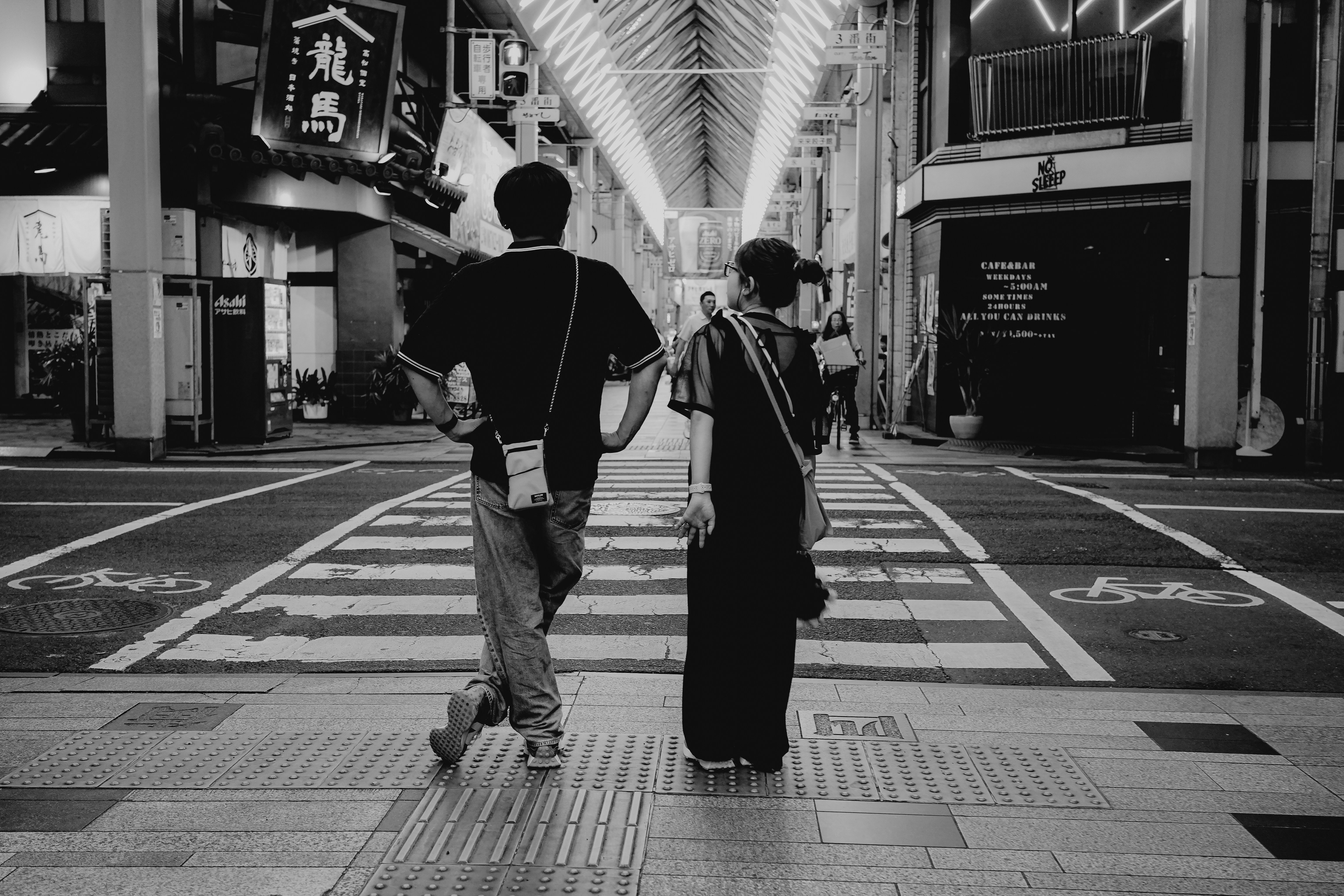 Two people walk across a crosswalk at night.