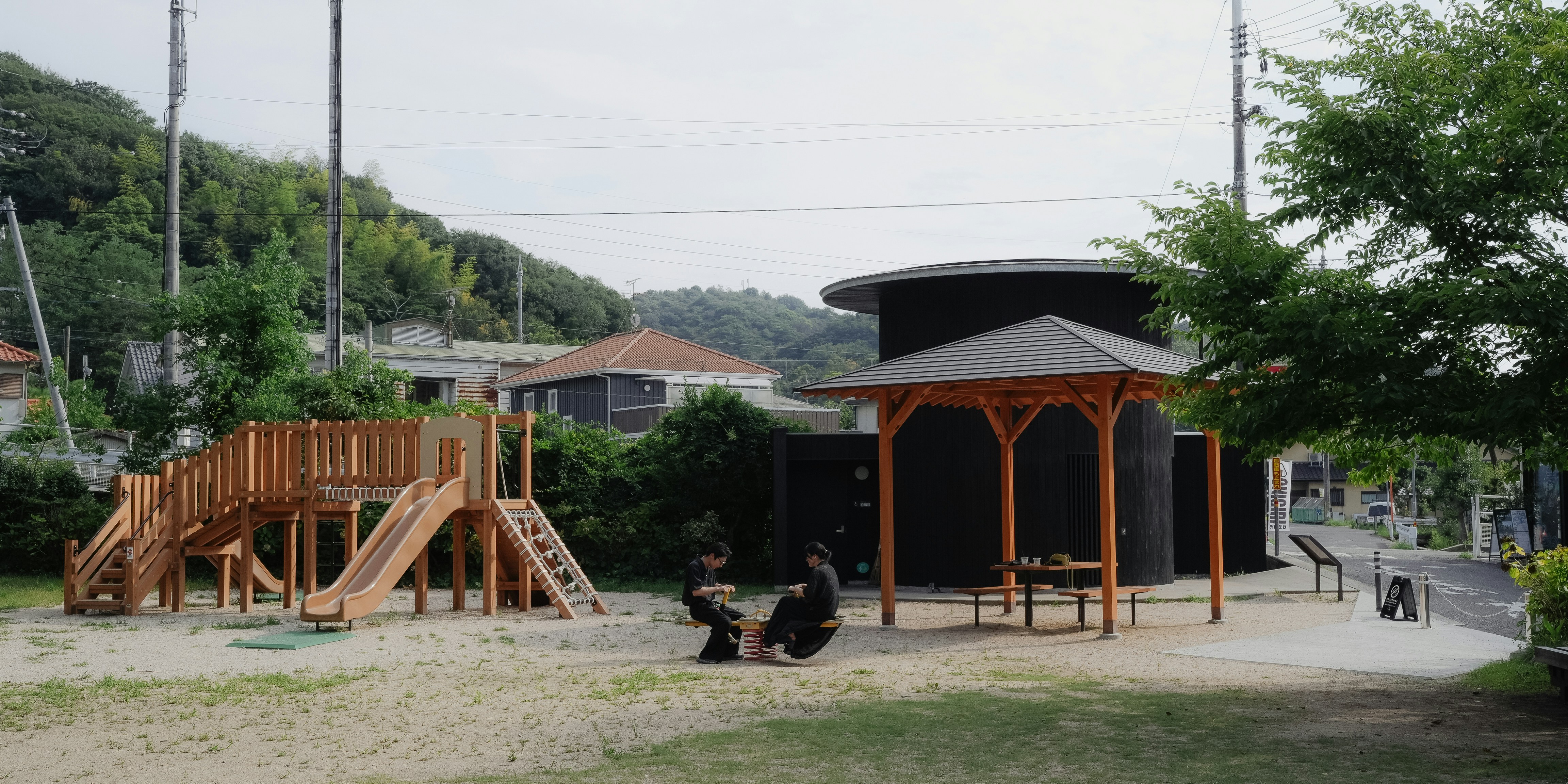 Wooden playground structure with a gazebo and two people.