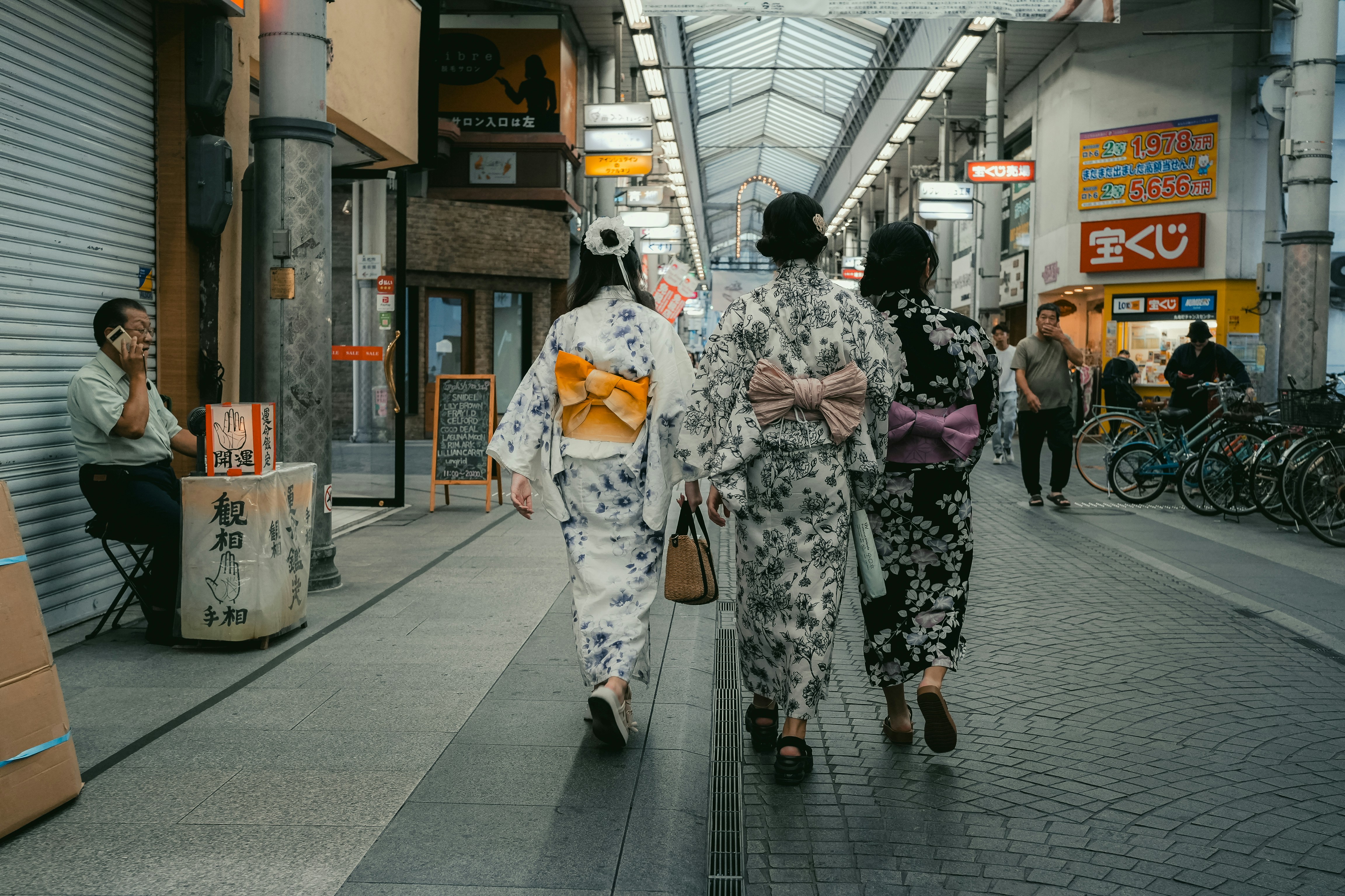 Three women in kimonos walk down a japanese street.