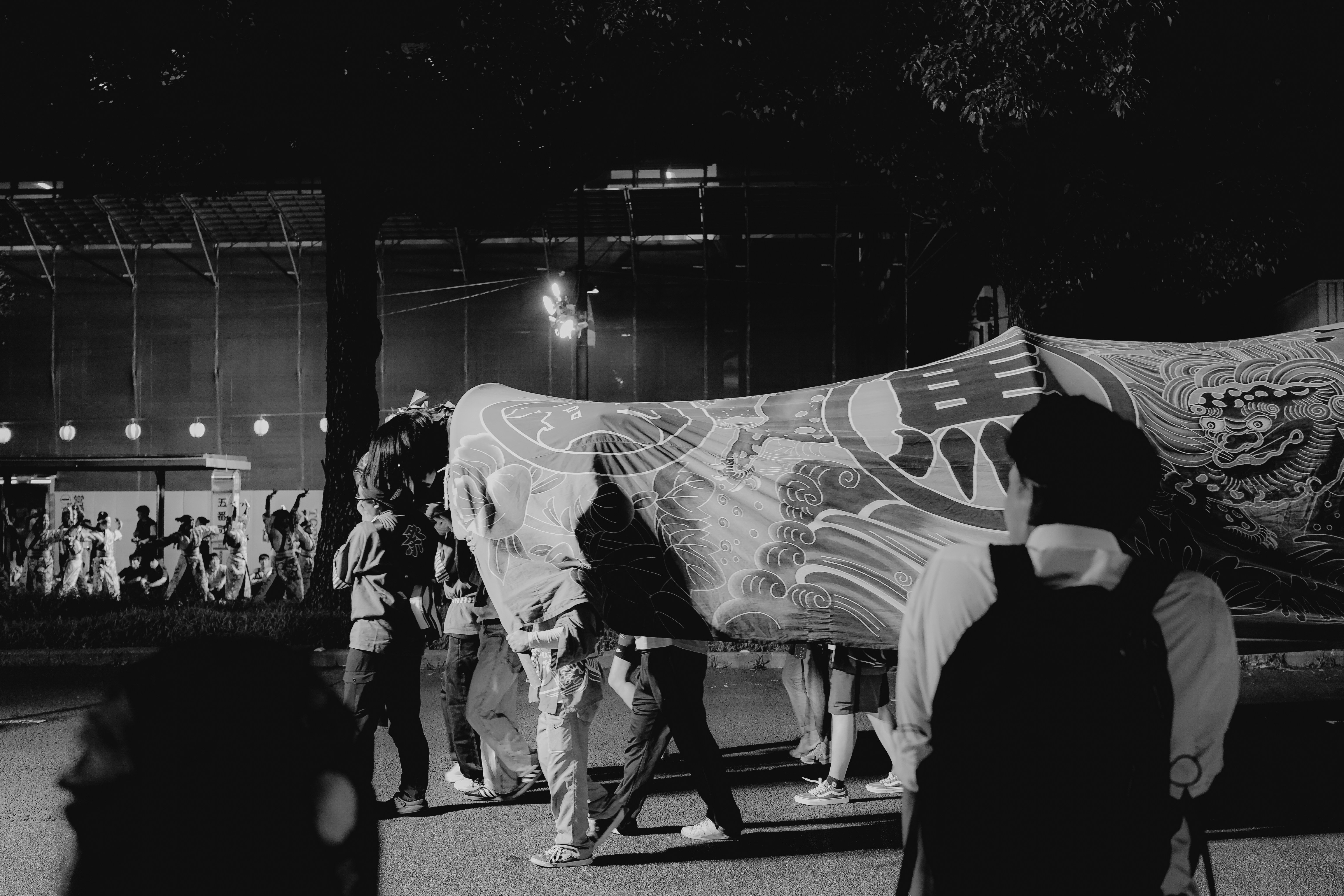 People carry a large decorated banner at night.
