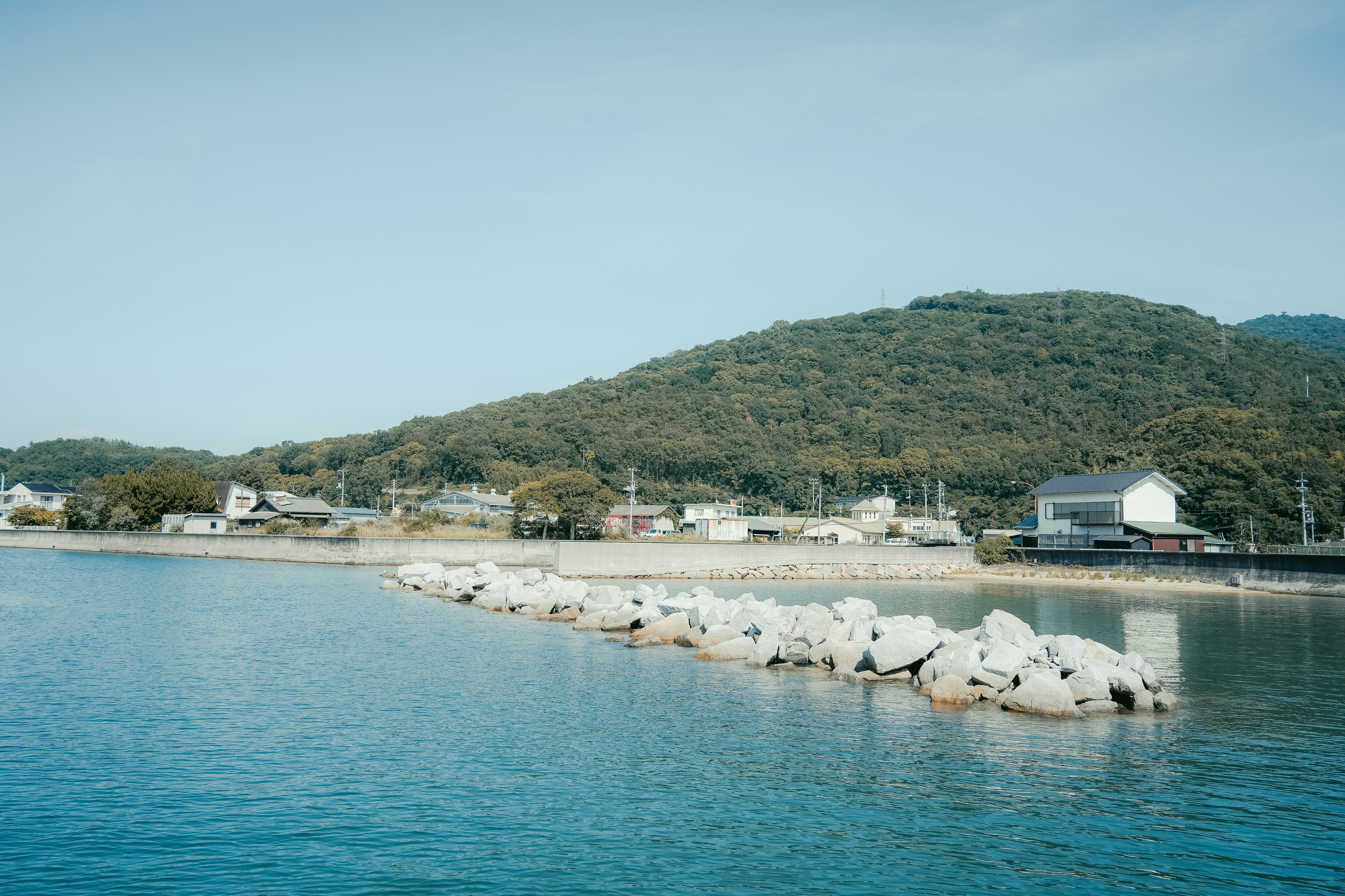 Coastal village with a breakwater and green hills.