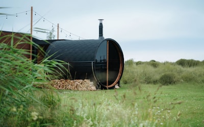 Barrel sauna with wood pile in grassy field.
