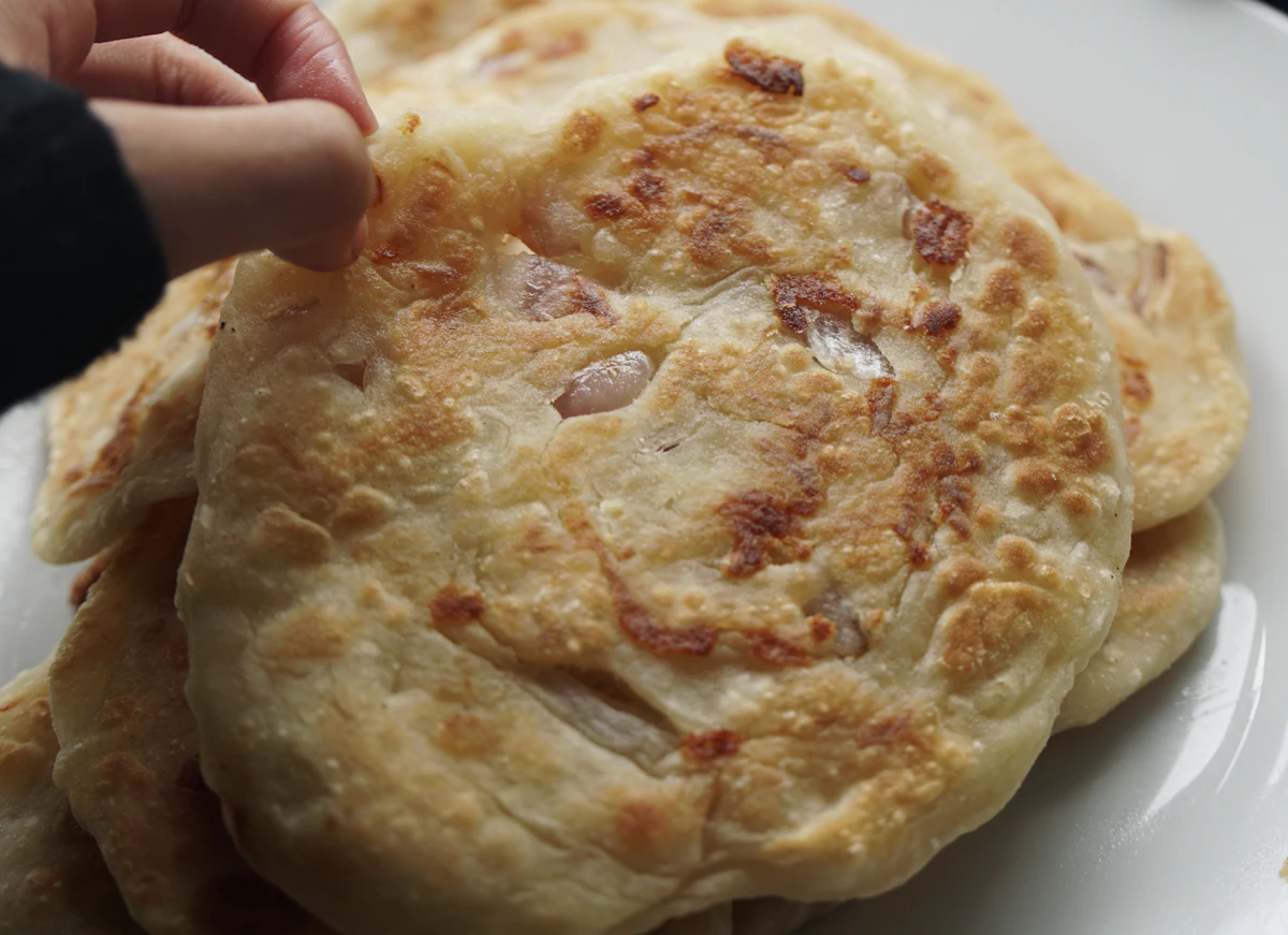 Bàn tay nhấc miếng bánh hành pajeon giòn - so sánh với bindaetteok