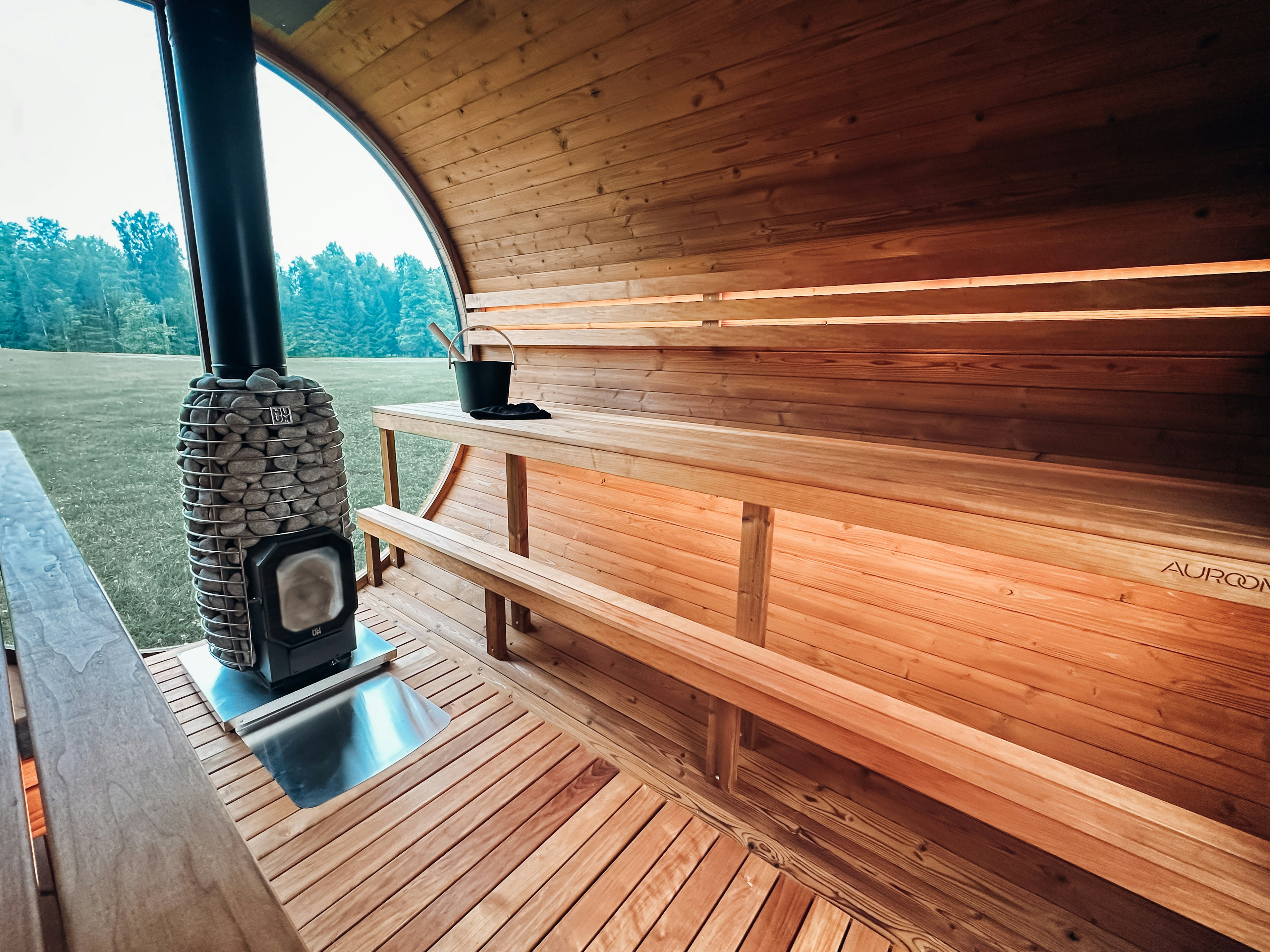 Wooden sauna interior with two levels of benches and a central stone-filled heater near a large window