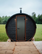 Barrel sauna with a door and chimney outdoors.