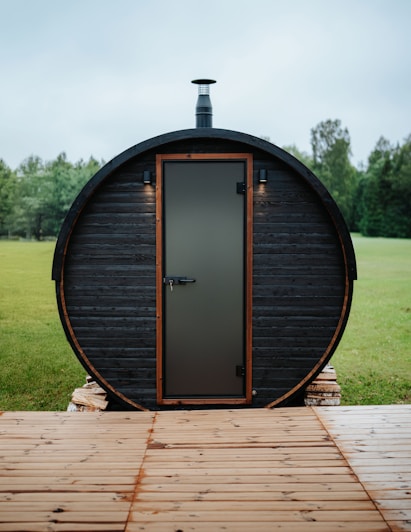Barrel sauna with a door and chimney outdoors.