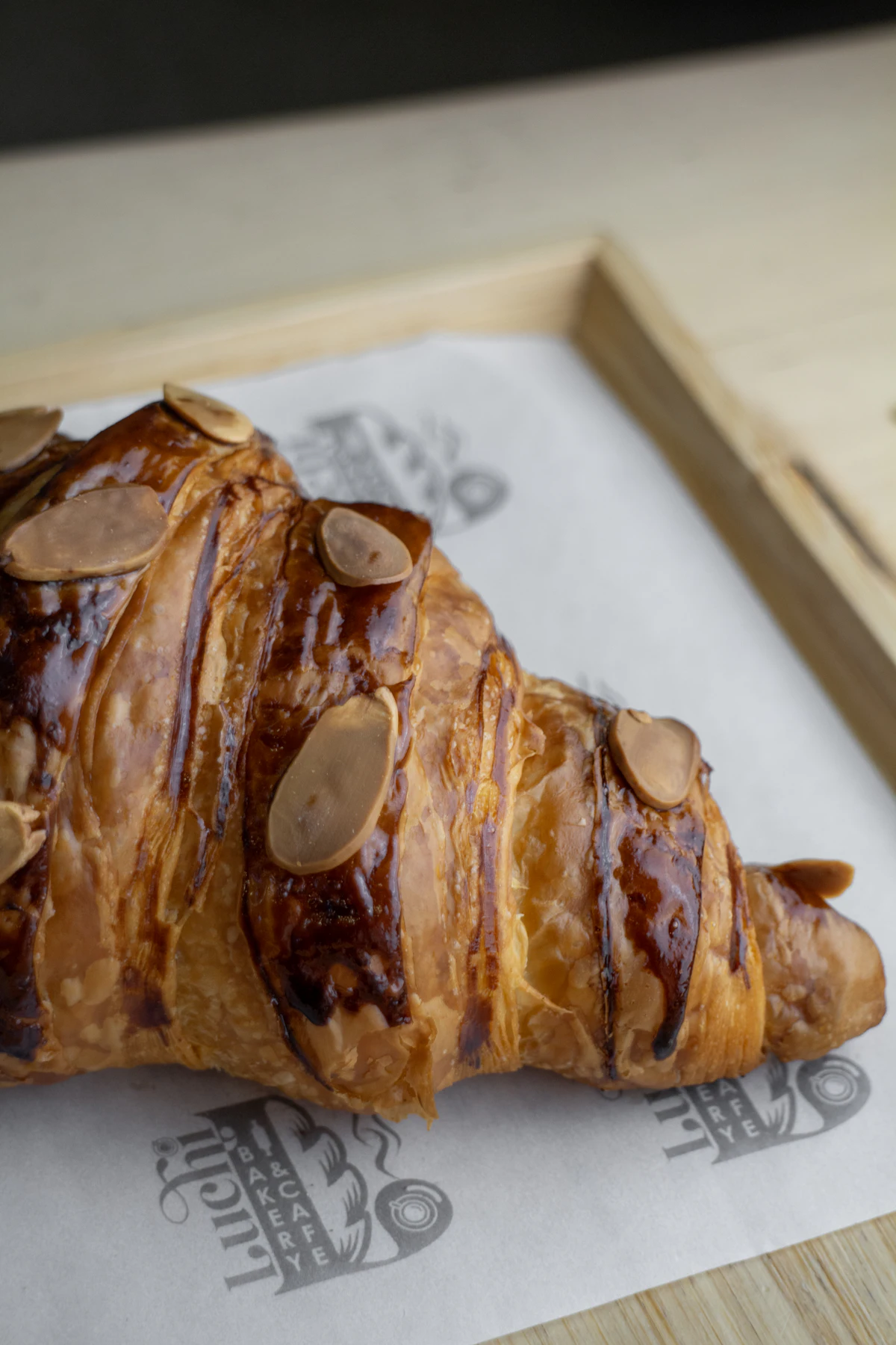 Almond croissant on paper with a wooden tray