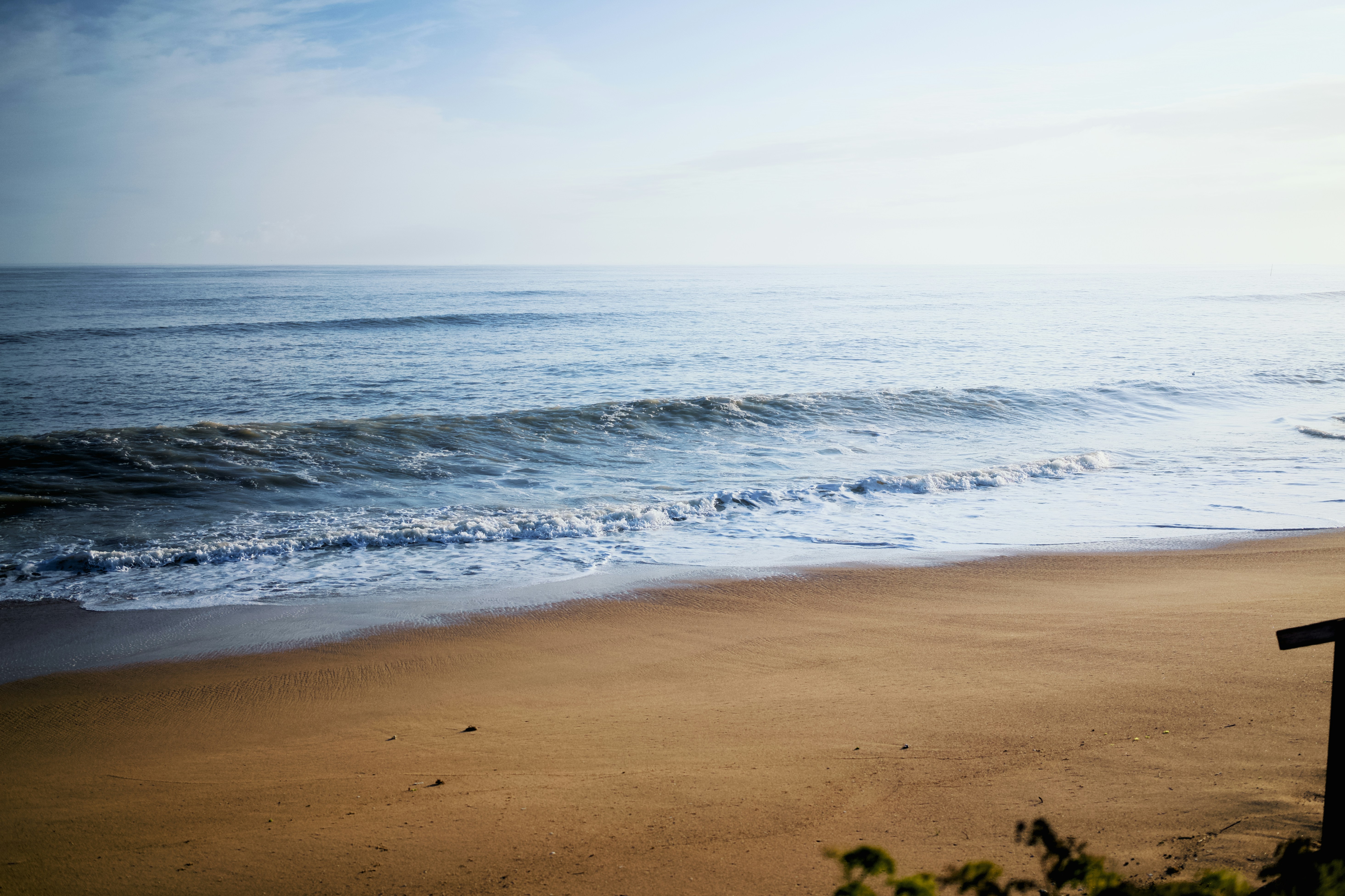 Gentle waves lap a sandy beach under a pale sky.