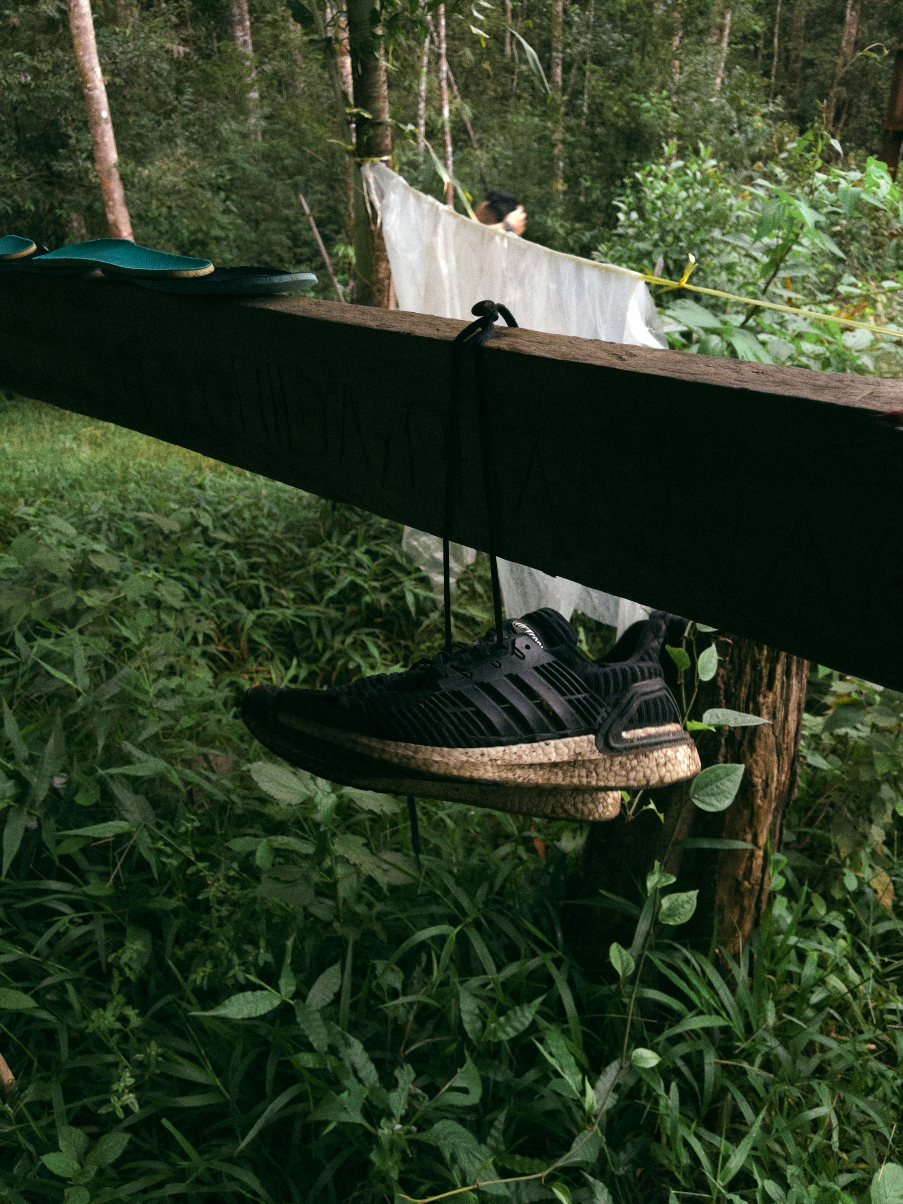 A single black sneaker hangs from a wooden beam.