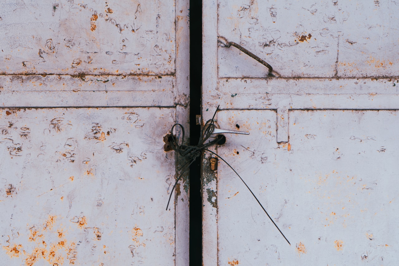 Weathered white metal double doors held shut by a twist of thin wire