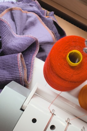 Spool of orange thread with purple fabric and sewing machine.