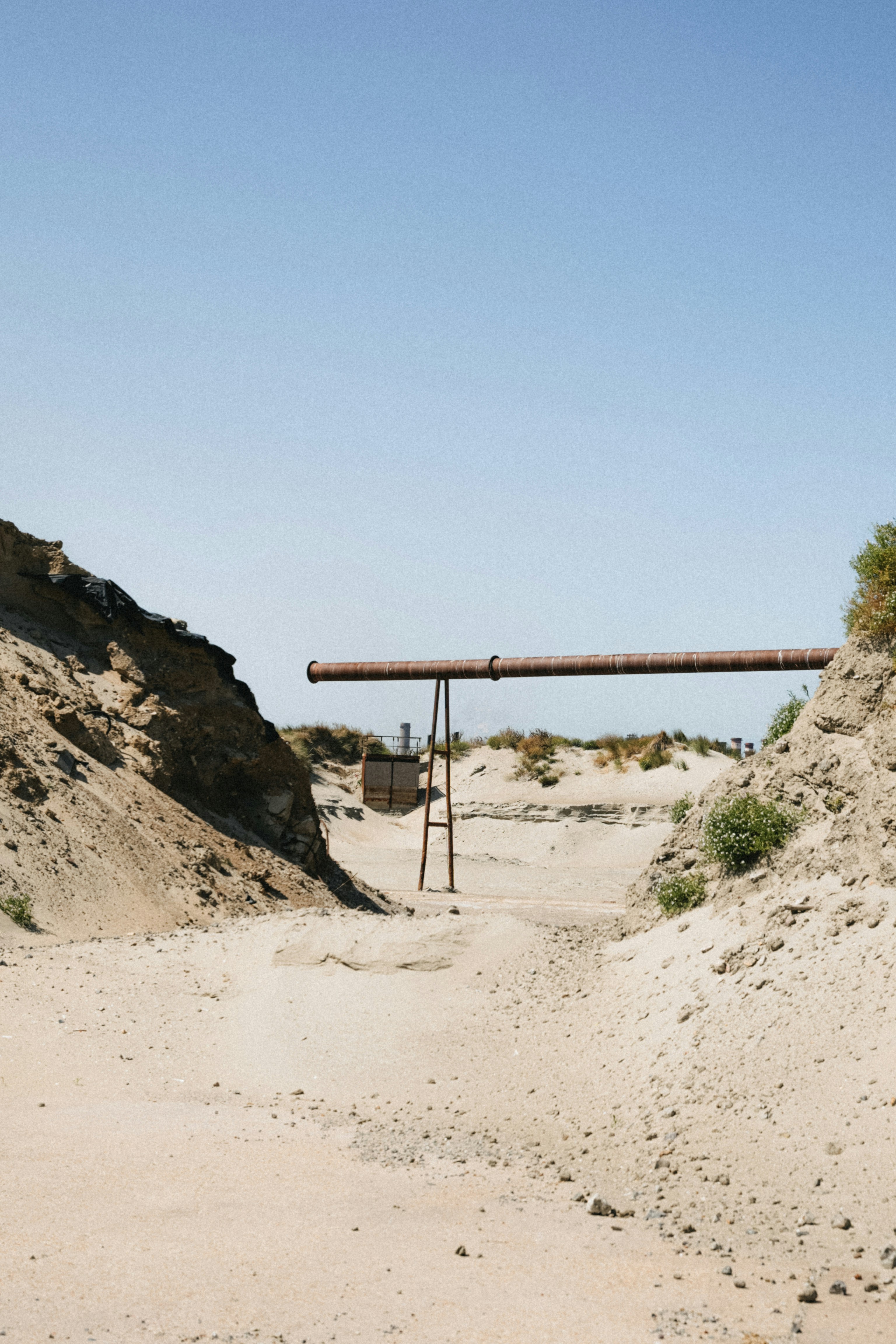 Rusty pipe crosses a dry, sandy landscape under clear sky.