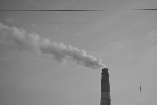 Smoke billows from a tall industrial chimney against sky.