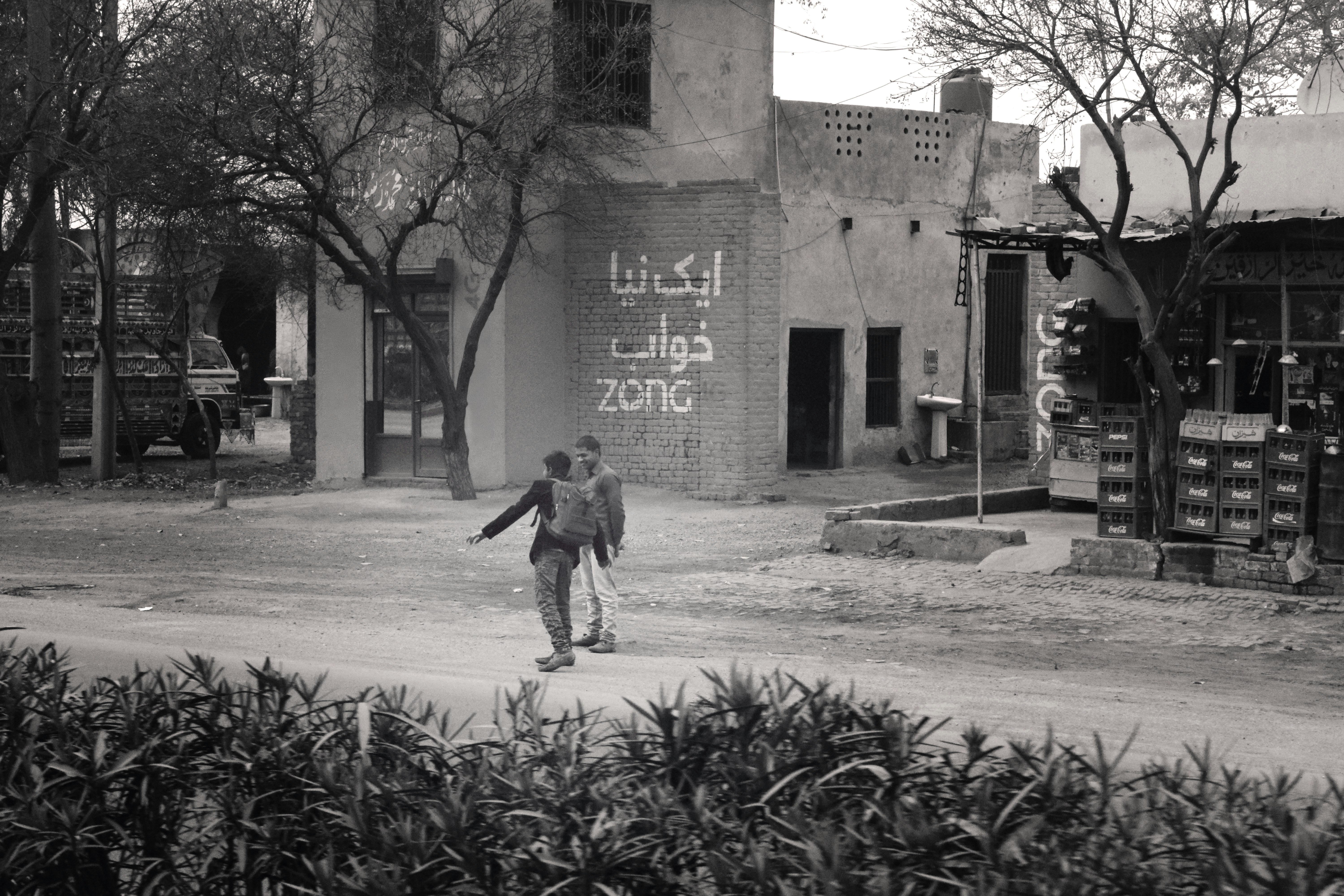 Two boys walking on a dusty street in a town.