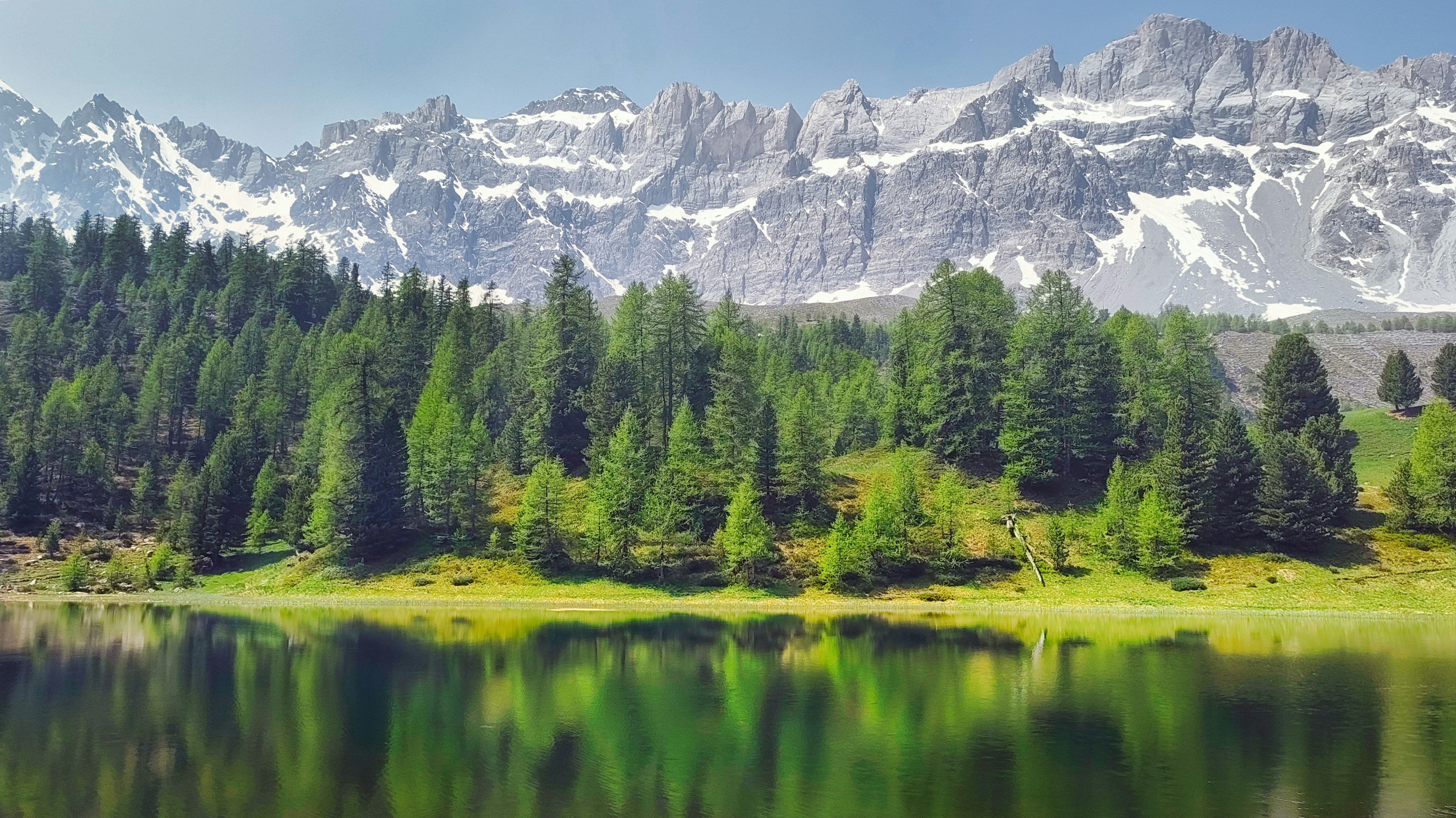 Snow-capped mountains overlook a serene forest and lake.