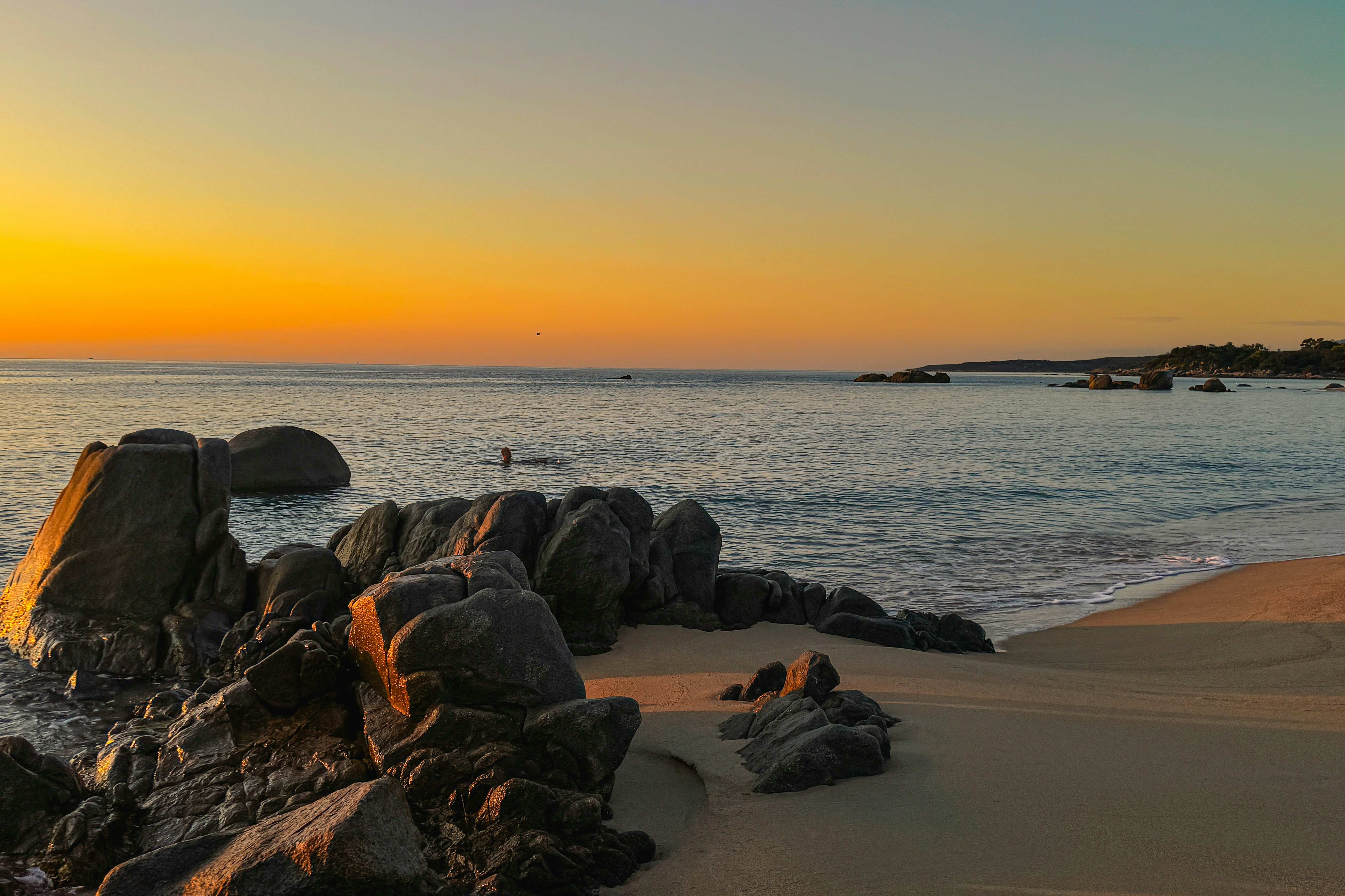 Golden sunset over a calm ocean with rocky shore.