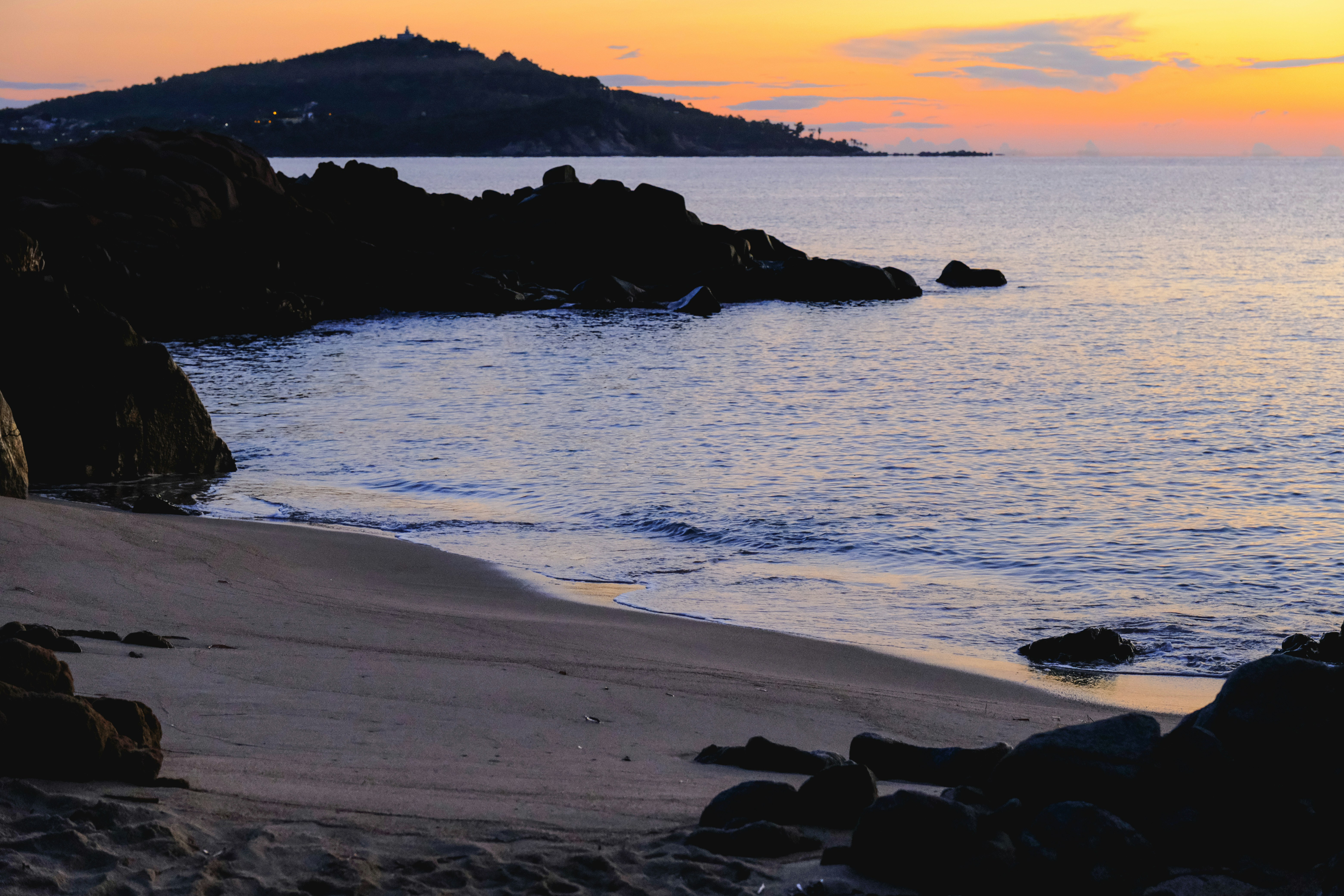 Calm ocean waves lap a sandy beach at sunset.