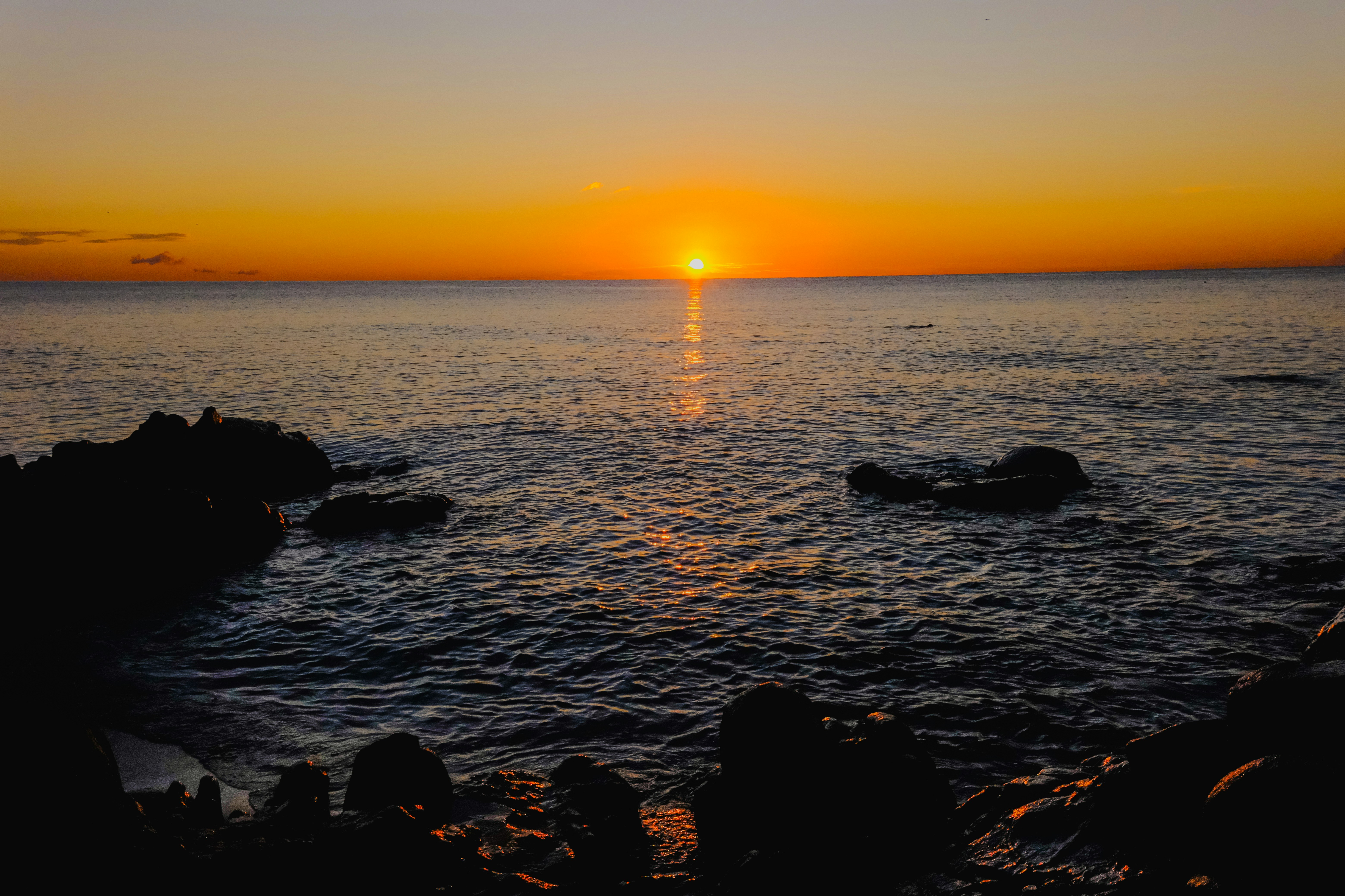 Sunset over a calm ocean with rocks.