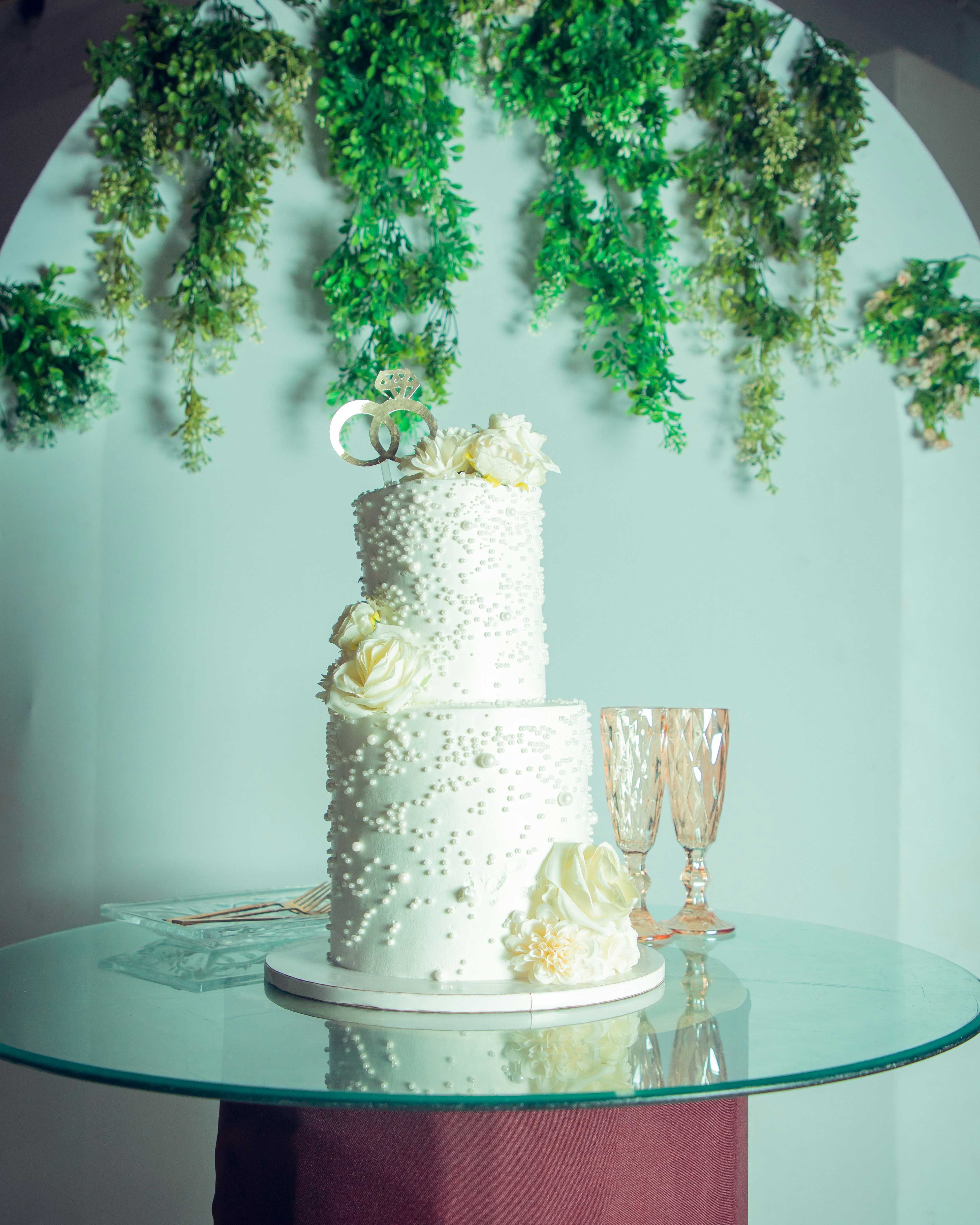 Elegant white tiered wedding cake with roses and champagne glasses.