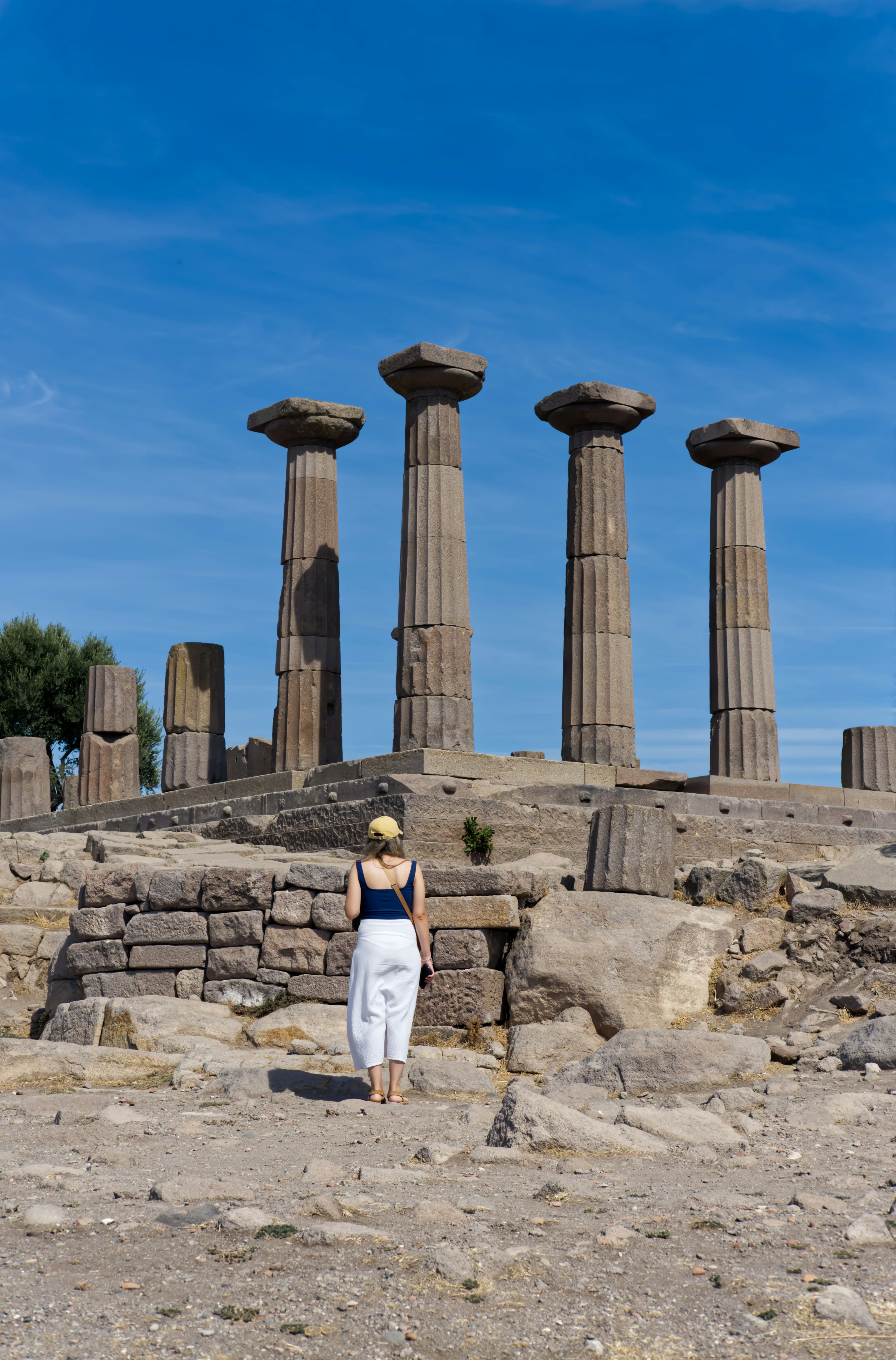 La donna si trova davanti ad antiche colonne di pietra sotto il cielo blu.