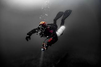 Scuba diver exploring dark underwater depths with bubbles.