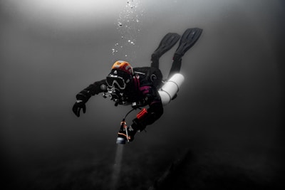 Scuba diver exploring dark underwater depths with bubbles.