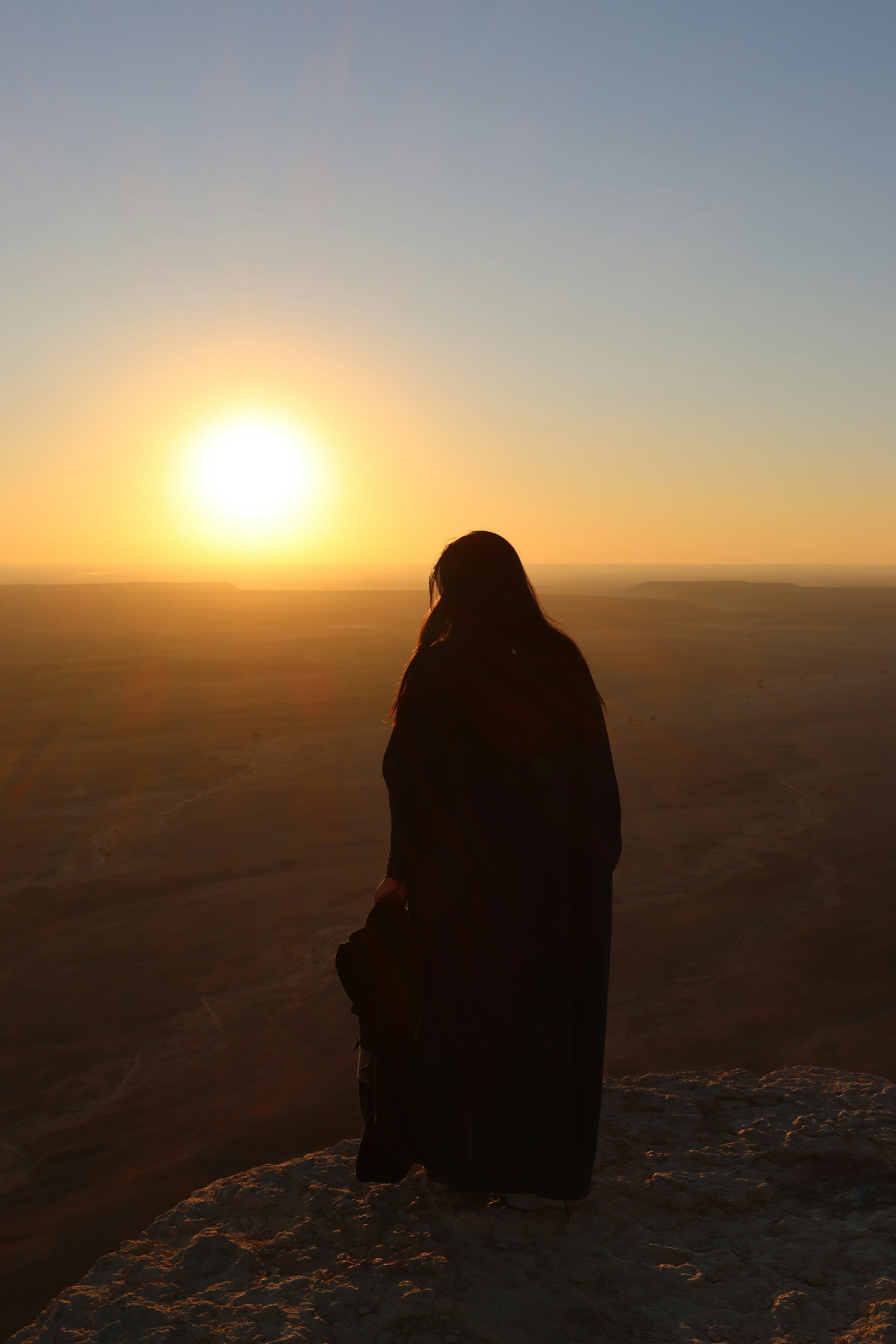 Persona viendo la puesta de sol desde un acantilado.