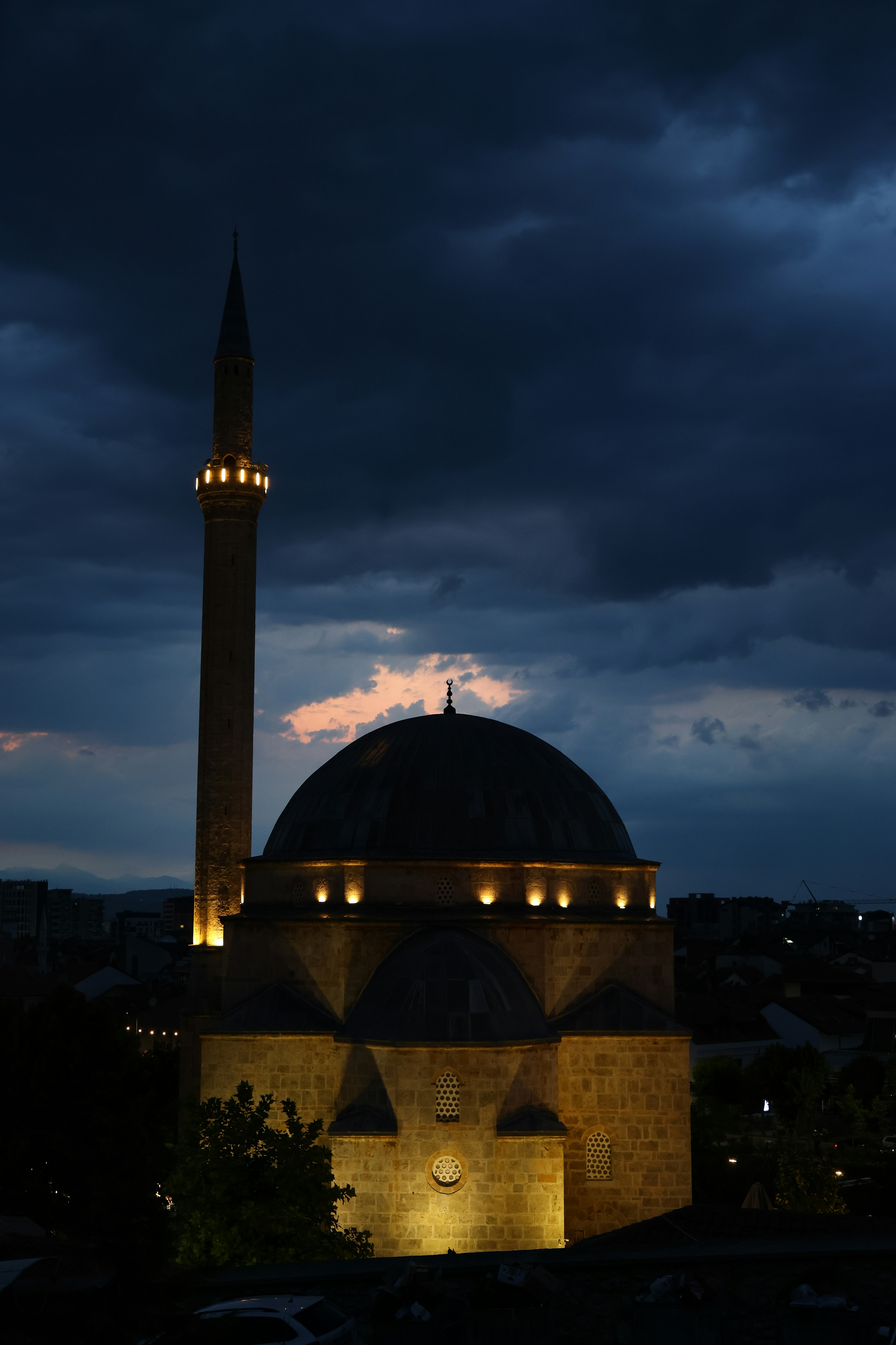Mezquita iluminada con un alto minarete contra un cielo tormentoso.