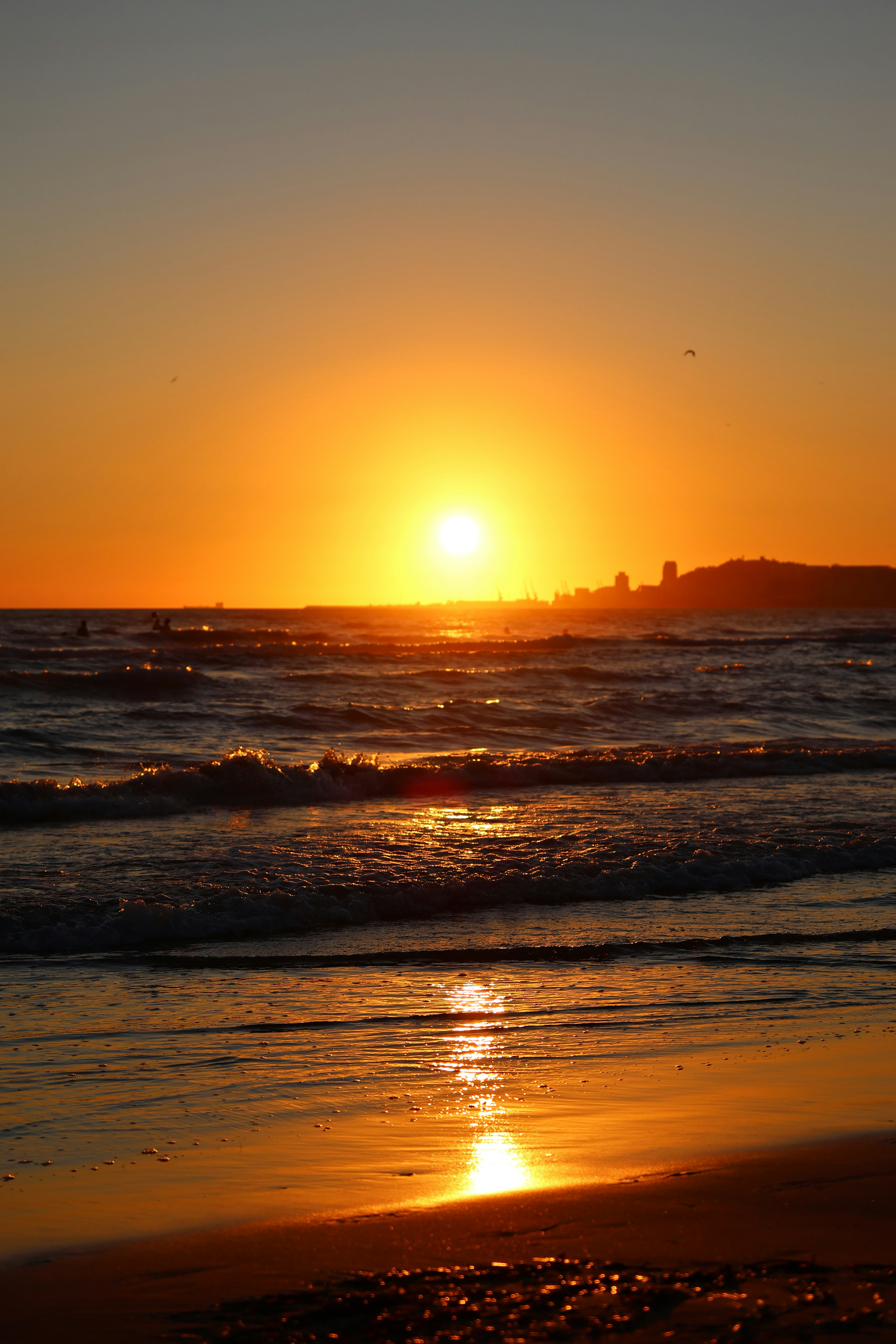 Atardecer dorado sobre un océano en calma con un horizonte de ciudad distante.