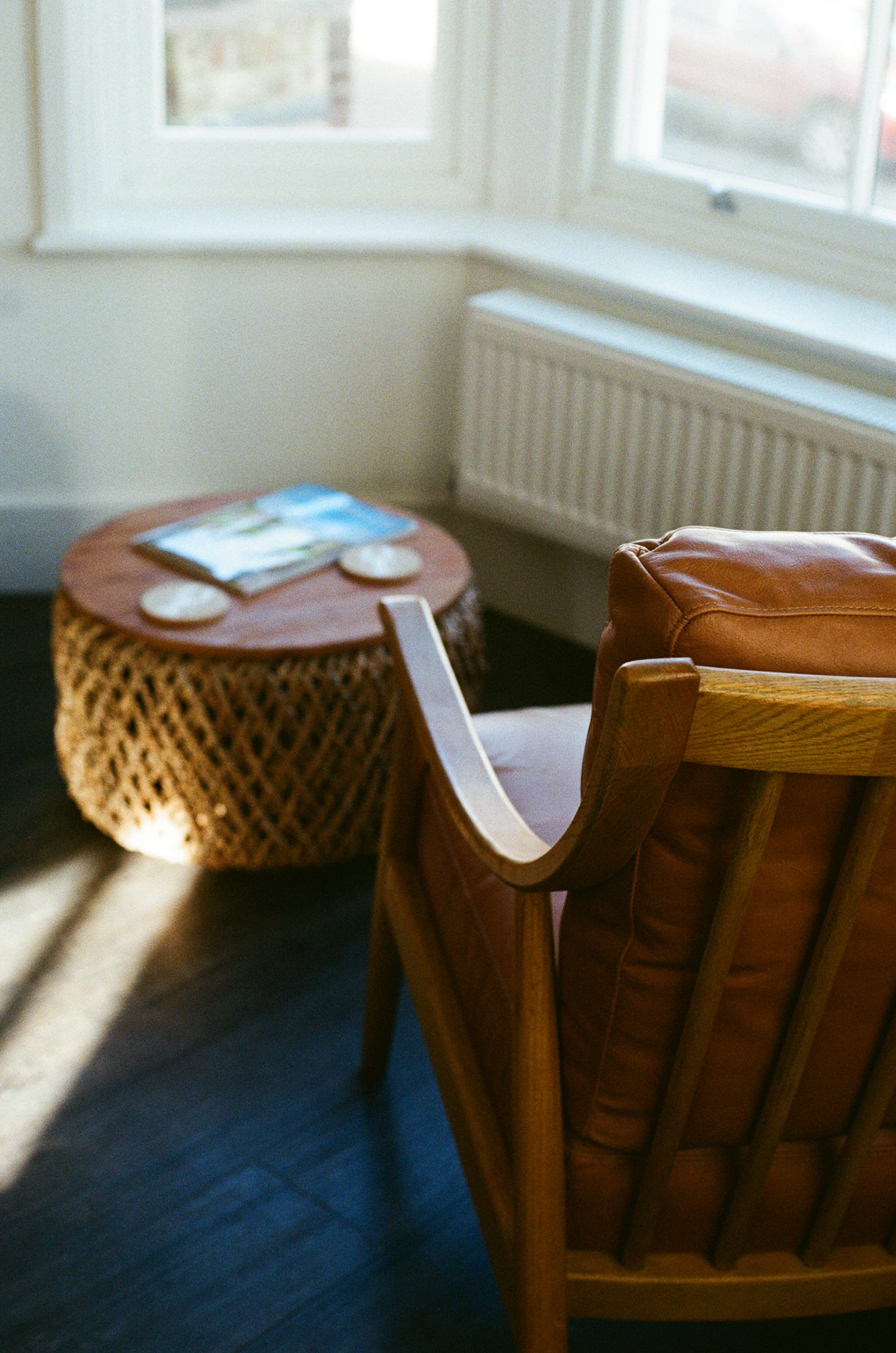 A leather armchair and a woven side table beside a bright window in the MANN studio