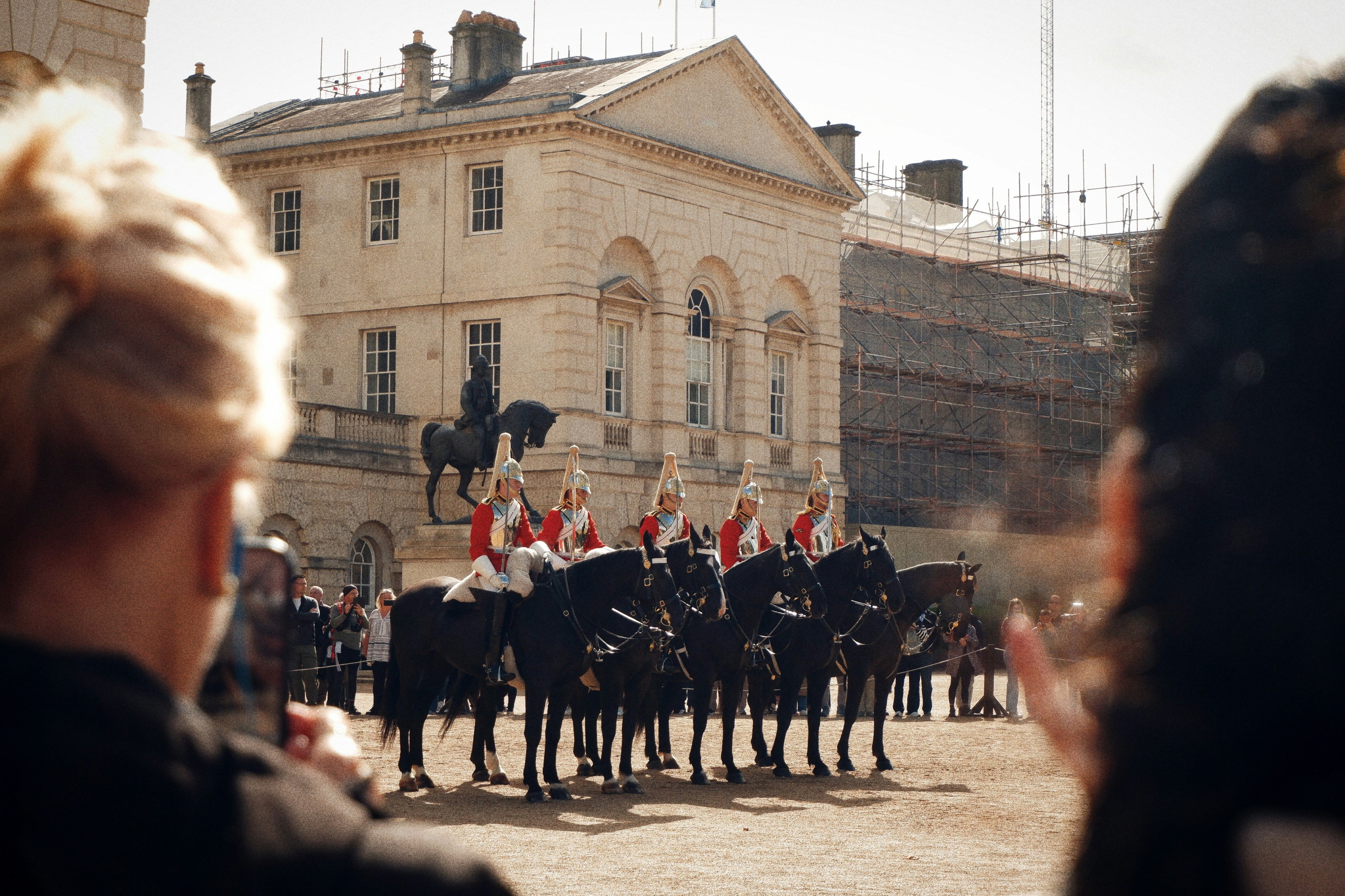 Horse guards in uniform on horseback outside building.