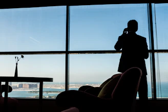 Man in suit talking on phone by large window.