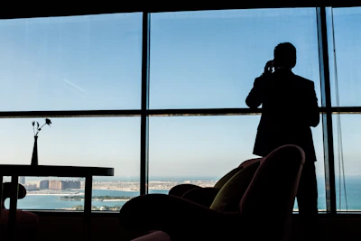 Man in suit talking on phone by large window.