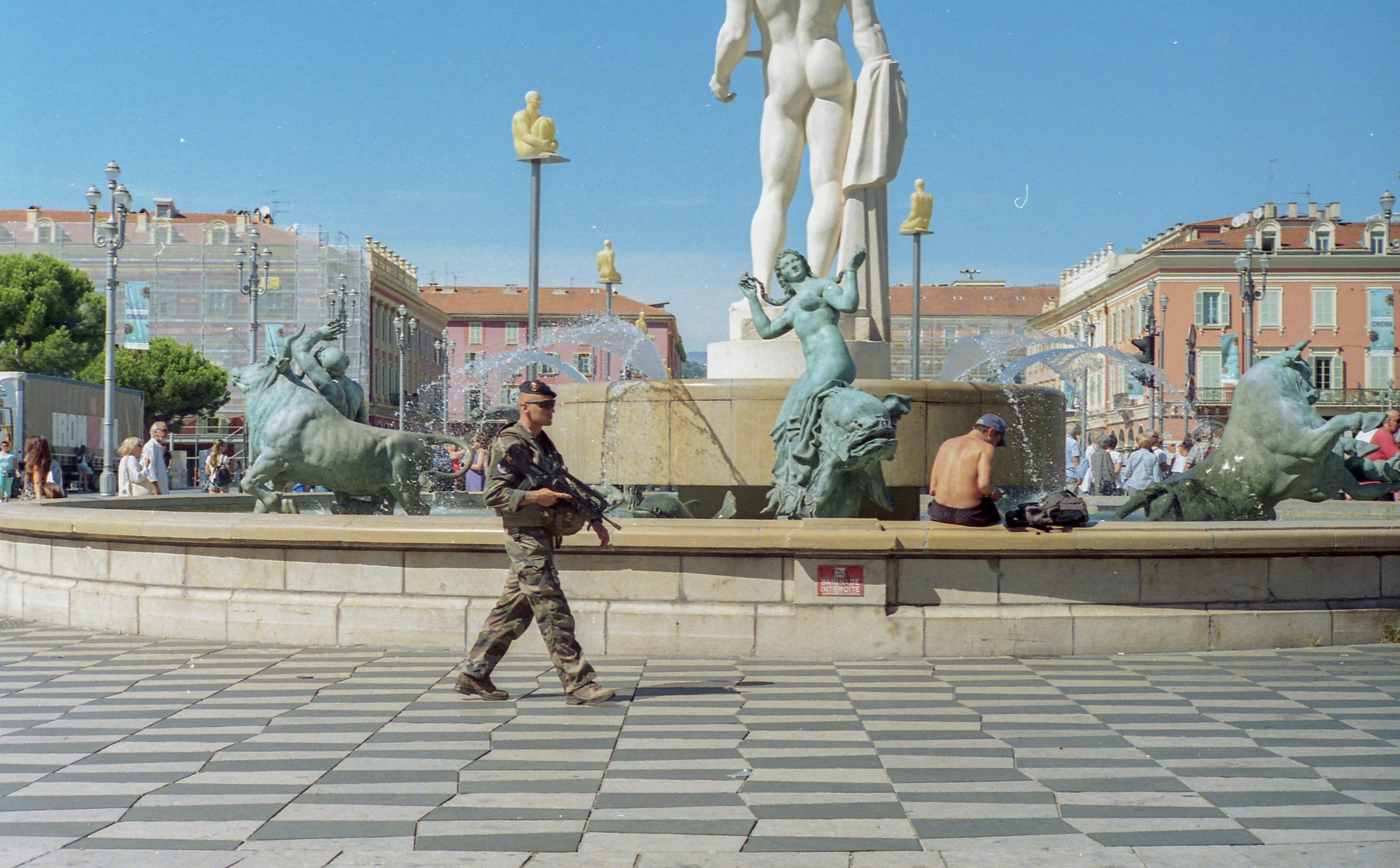 Soldier walks past a fountain with statues and people.
