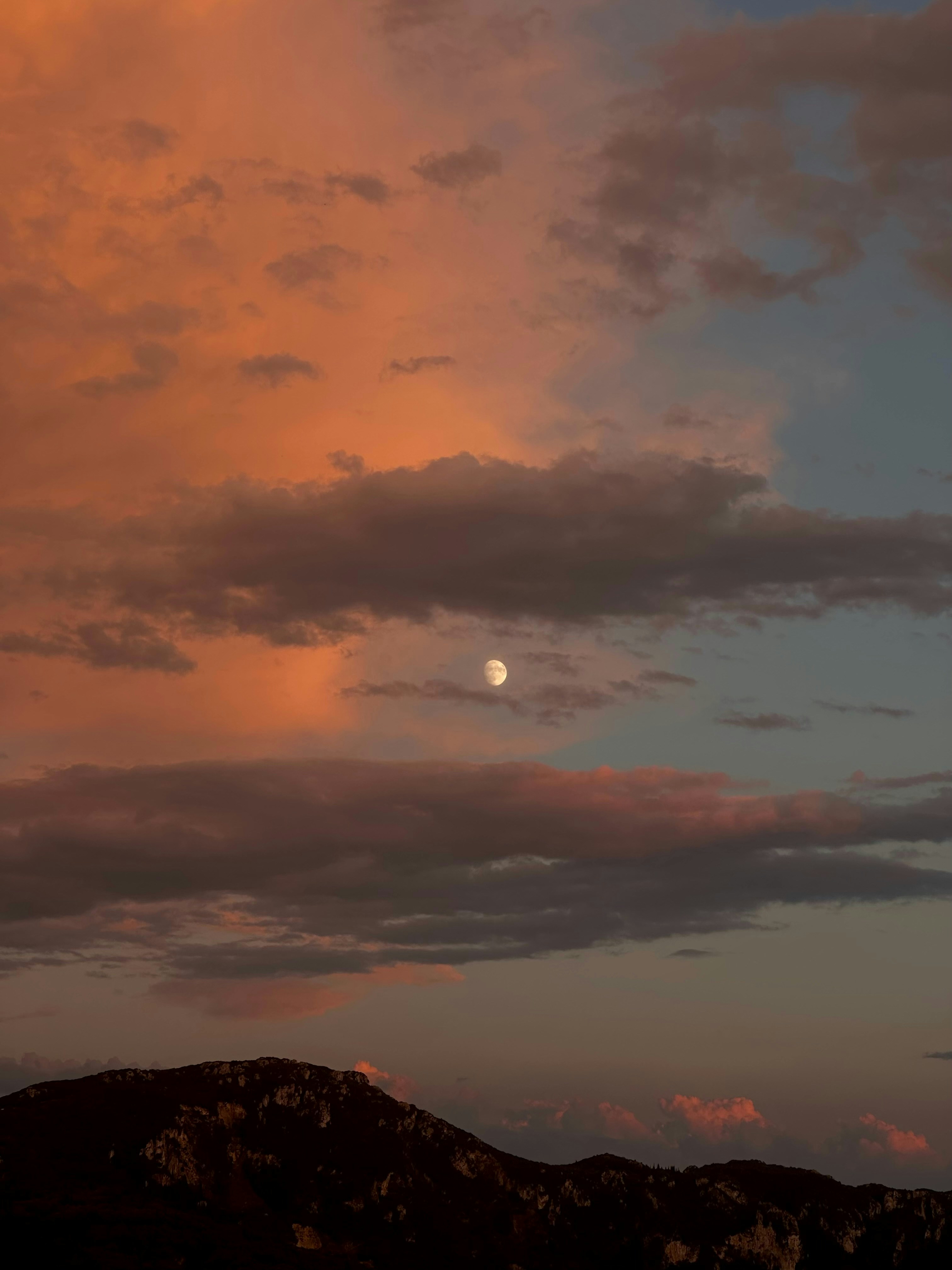 Lune visible dans le ciel nuageux sur la silhouette de la montagne