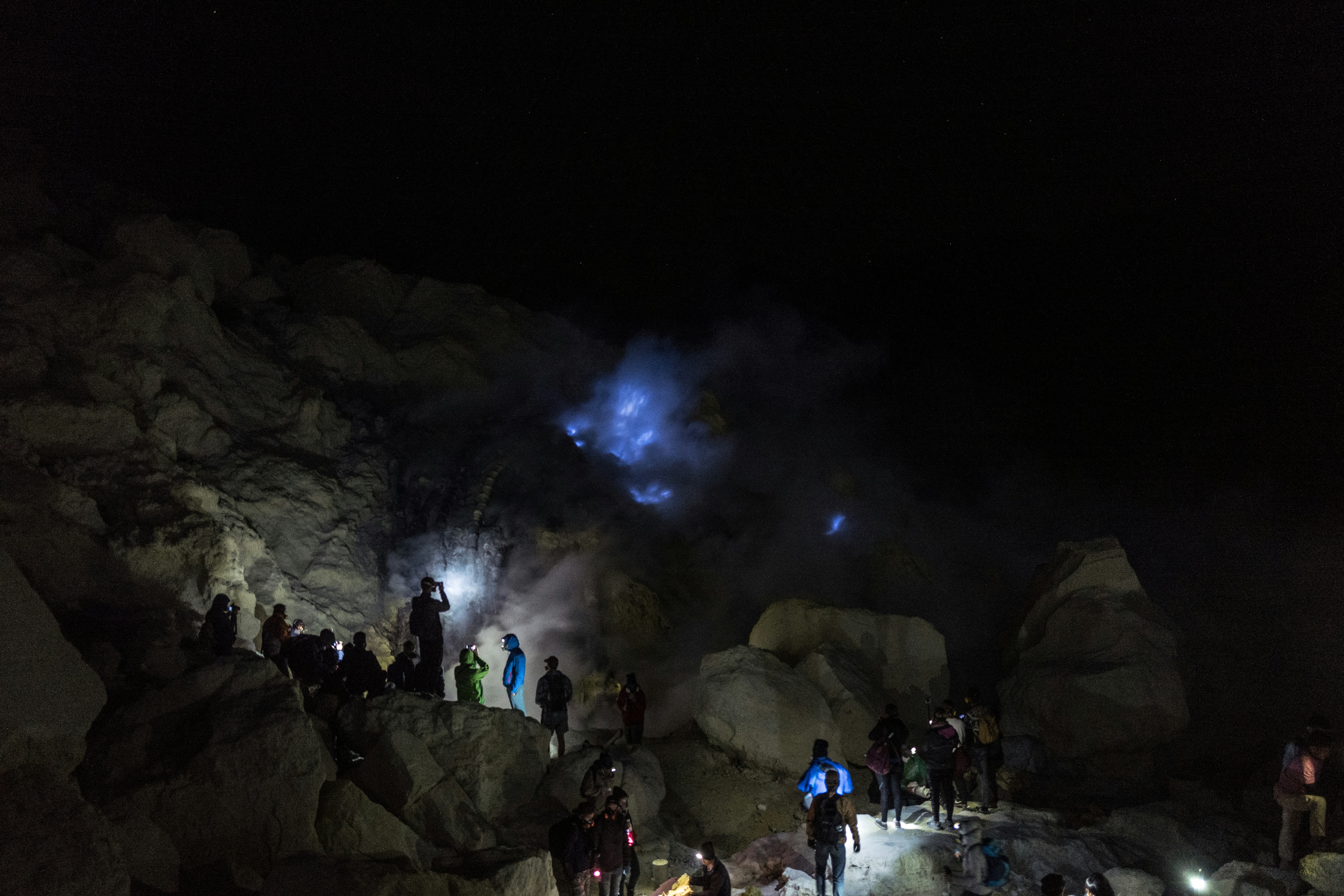 People observe blue flames on a rocky mountainside at night.