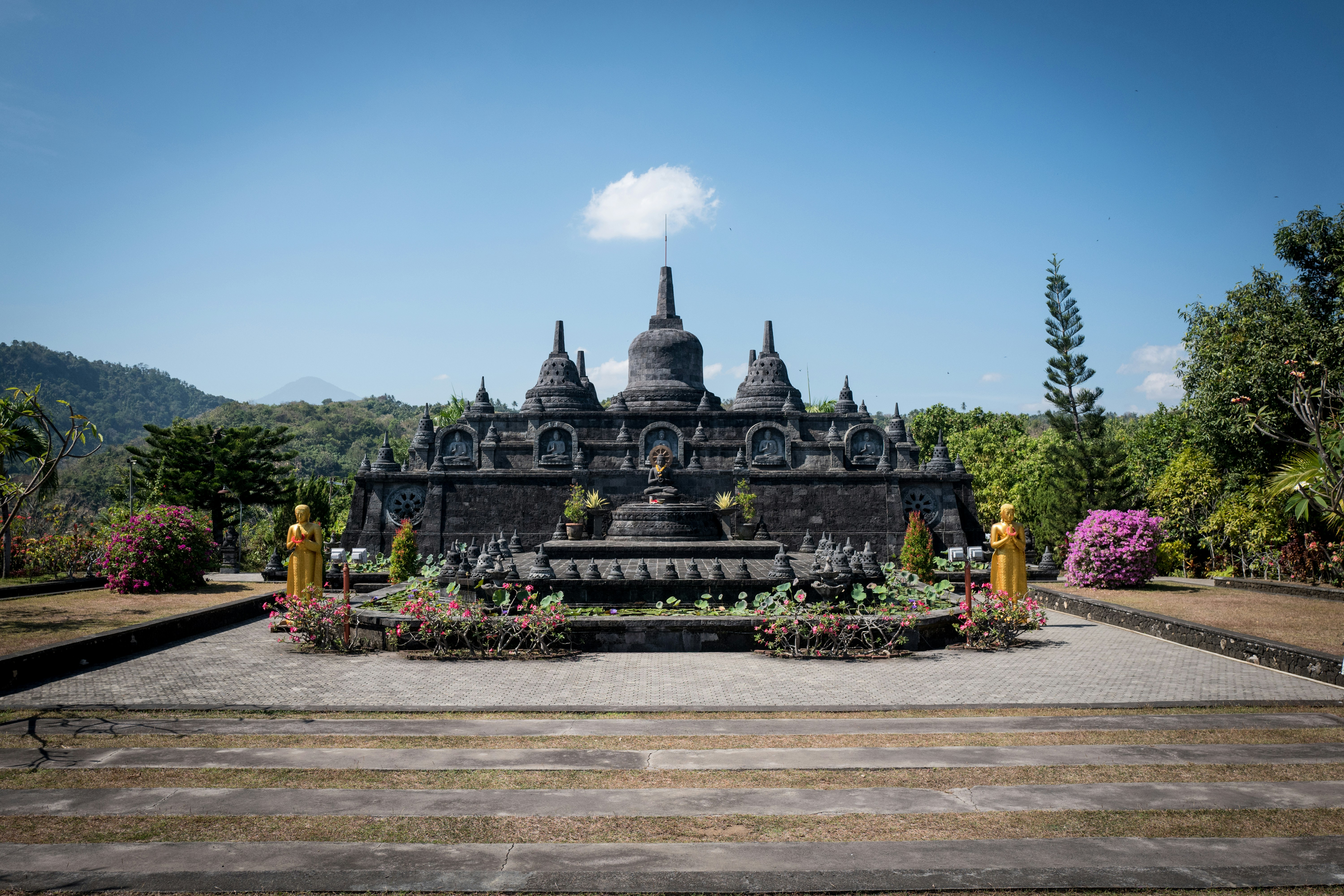 A dark stone buddhist temple with lush green surroundings.
