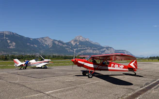 Two small airplanes parked on tarmac with mountains behind.